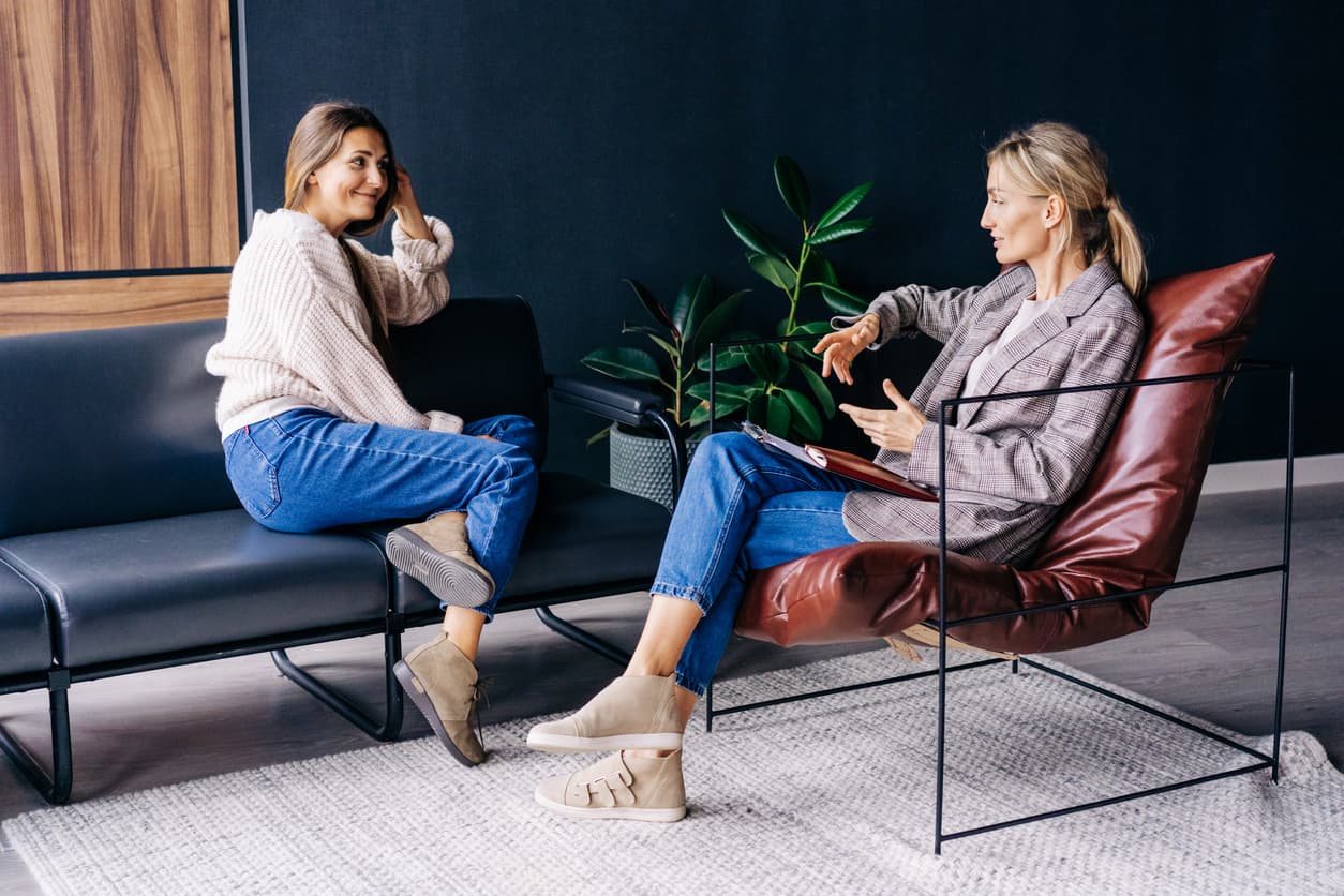 A smiling woman listens to the advice of a consultant psychologist sitting on a sofa in the workshop.