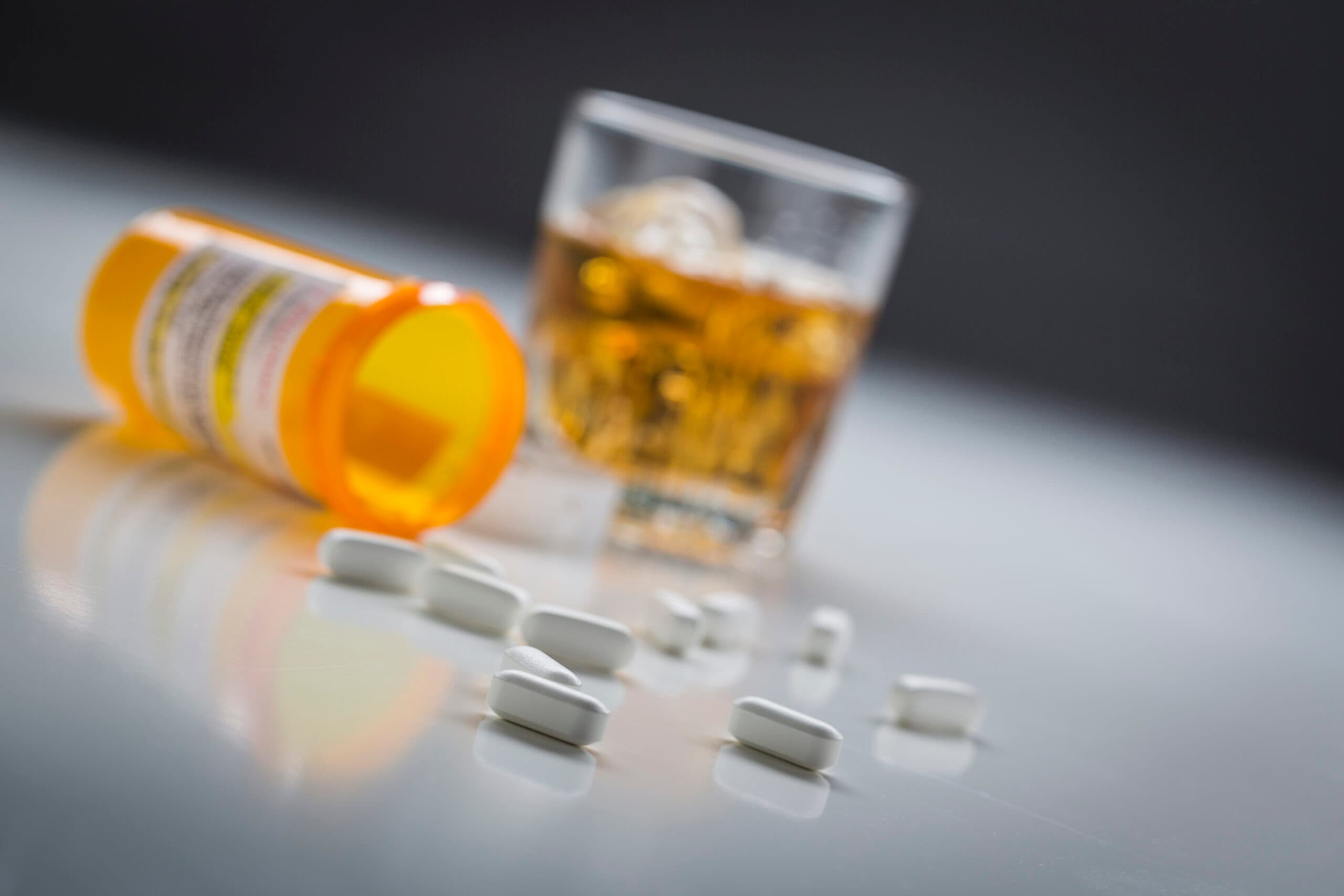 white prescription pills spilled out with glass of liquor