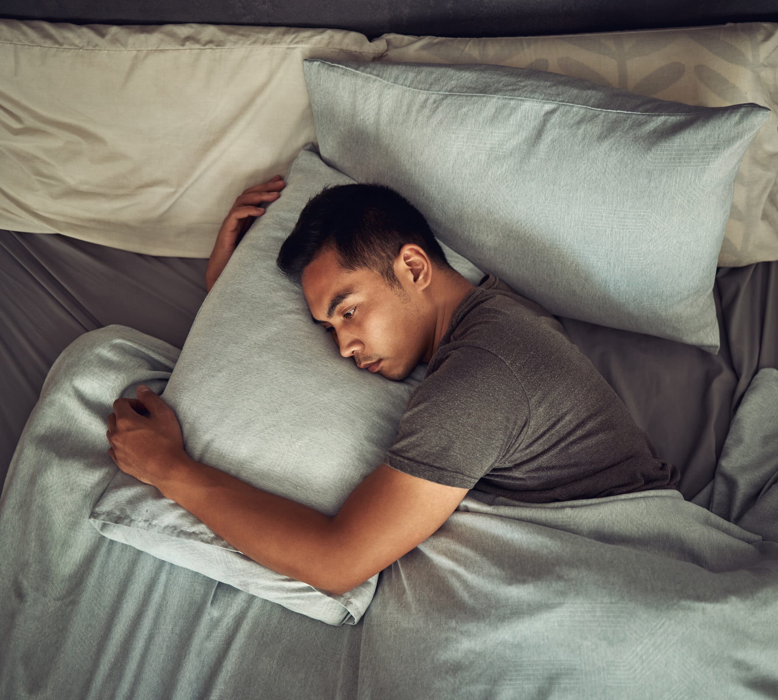 young man laying in bed head on pillow eyes wide open