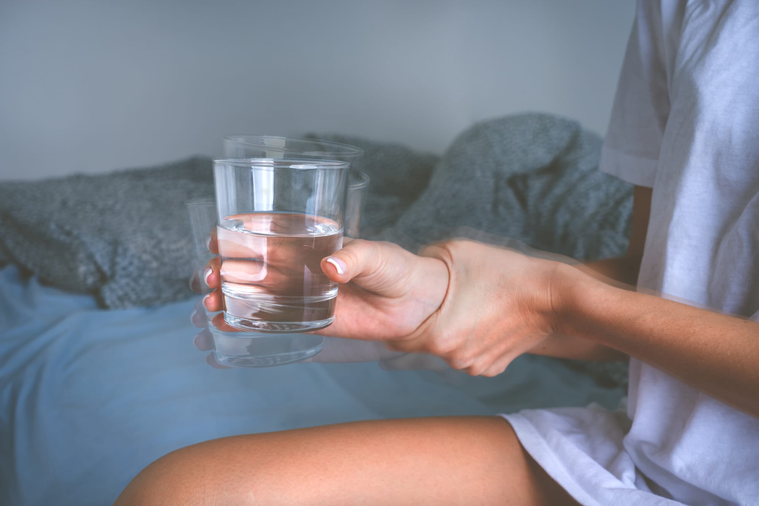 woman with shaking hands tremors water glass in bed