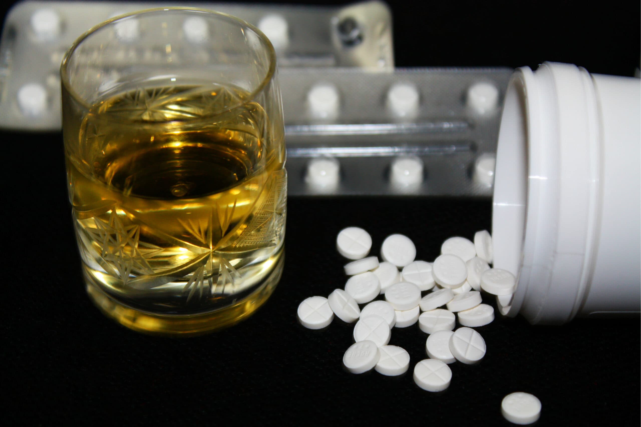 white pills spilled out with glass of liquor
