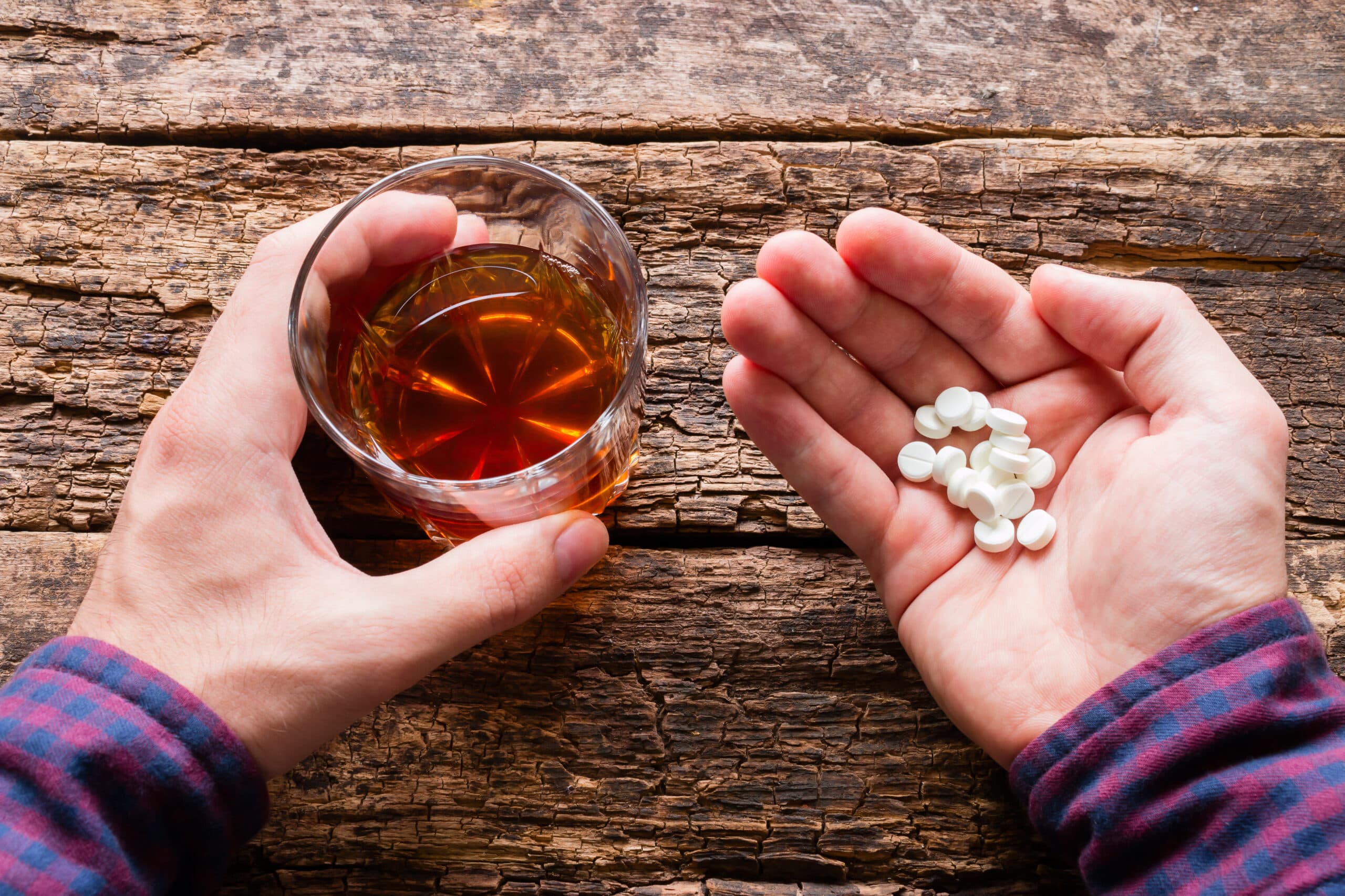 man holding glass of liquor and white pills