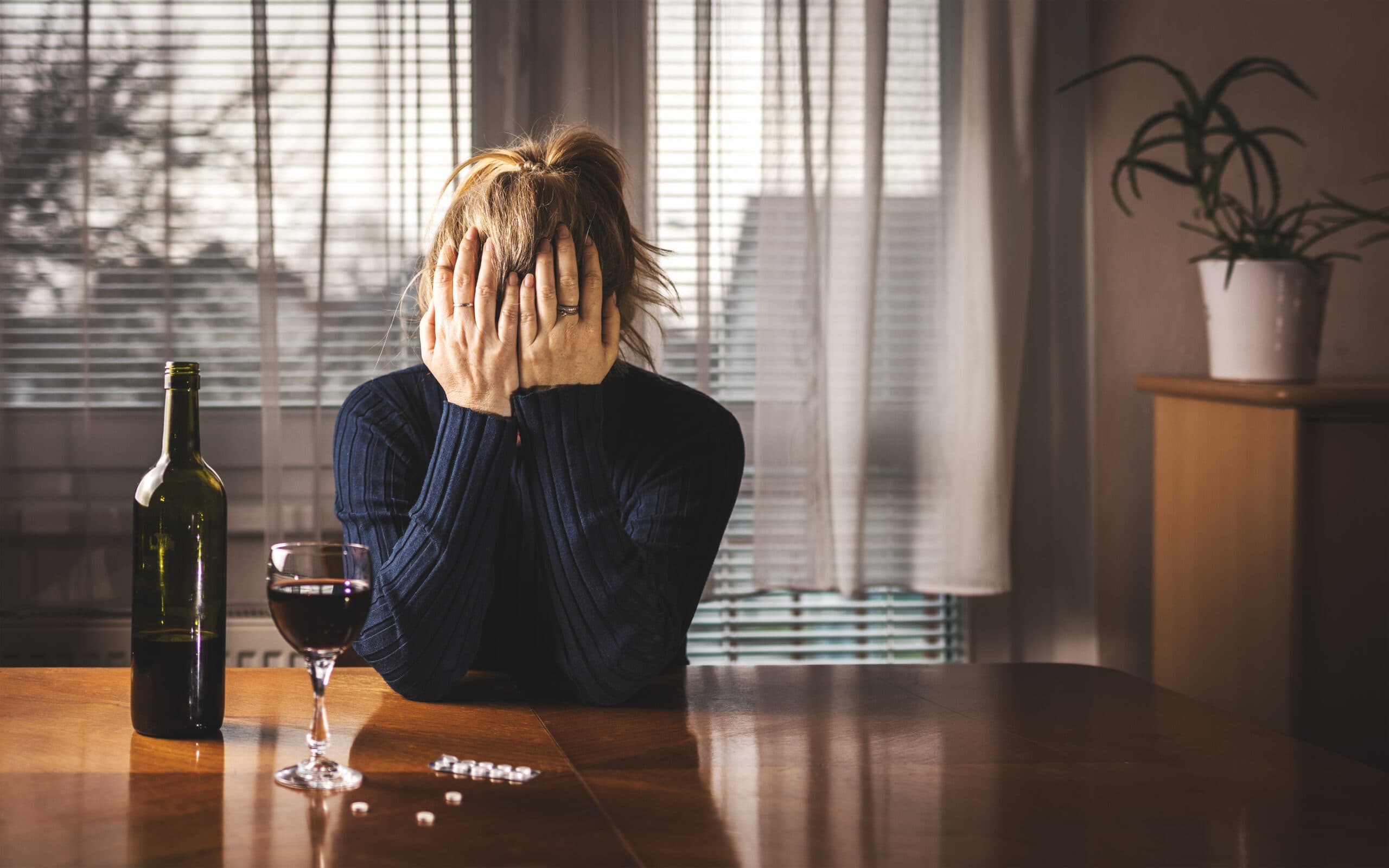 sad woman drinking wine and taking white pills