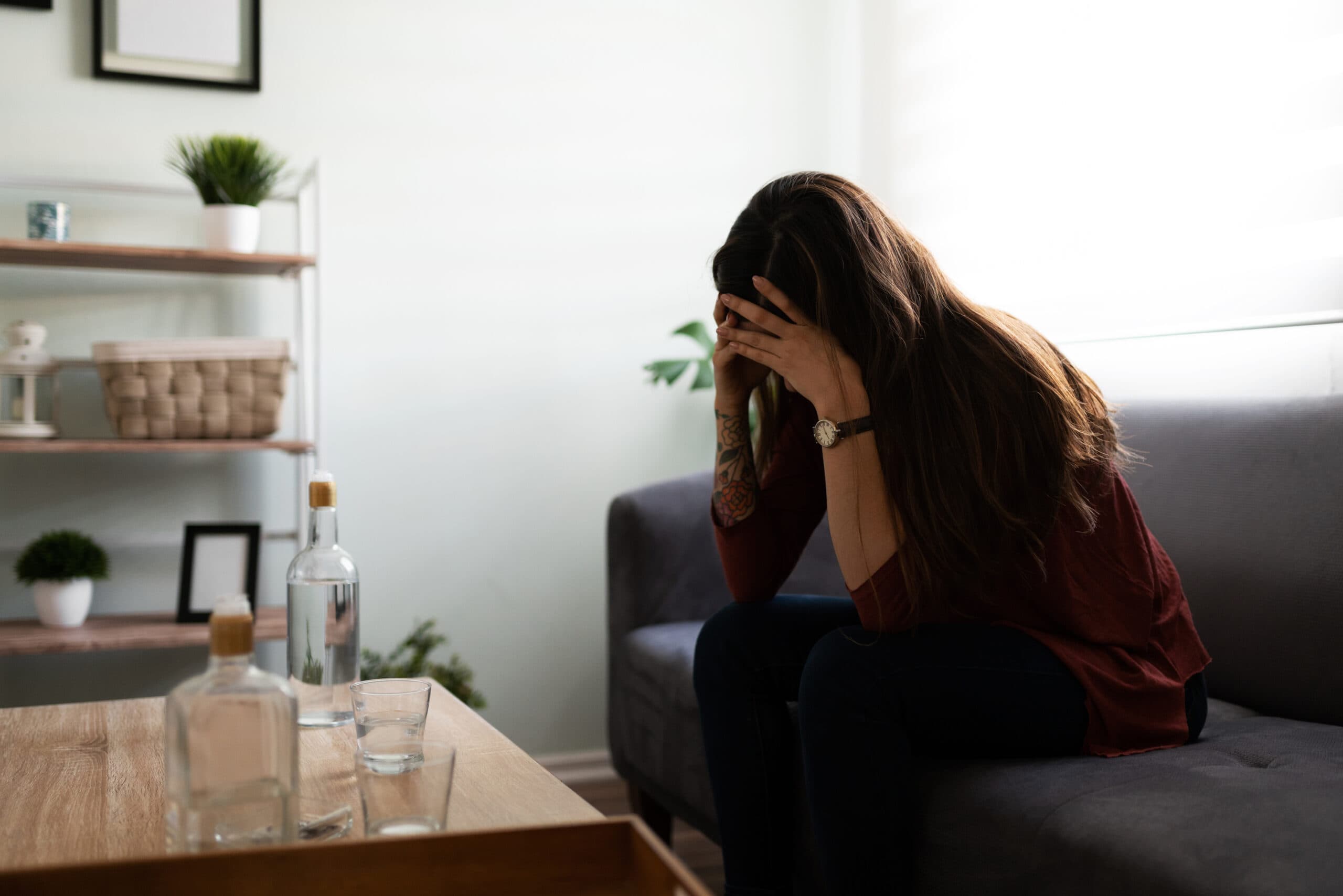 young woman alcoholic with liquor bottles upset