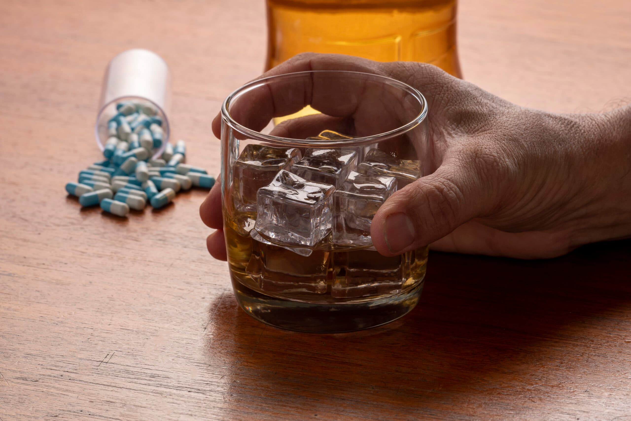 person holding glass of liquor with blue pills