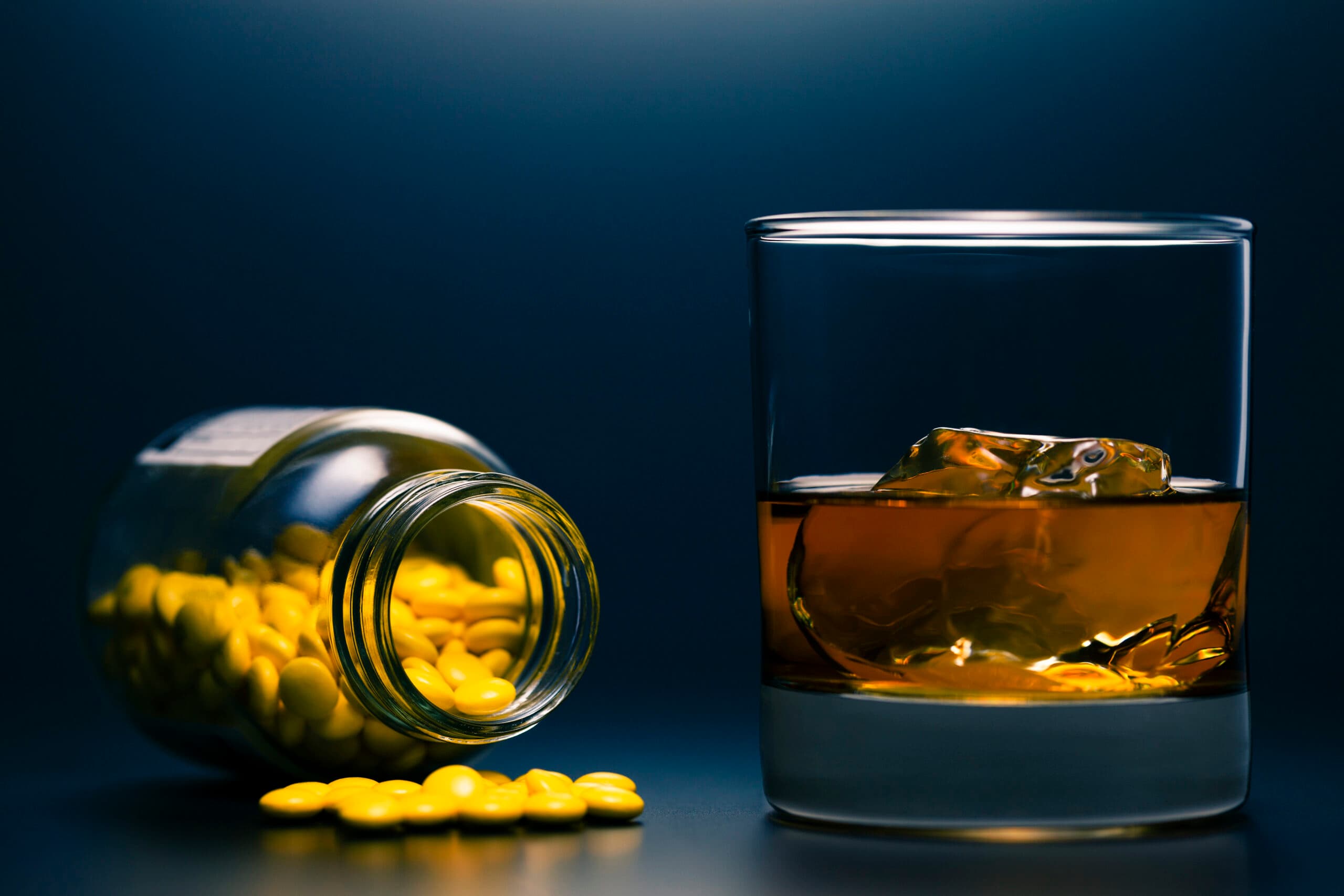 liquor drink in glass with pills spilled from bottle