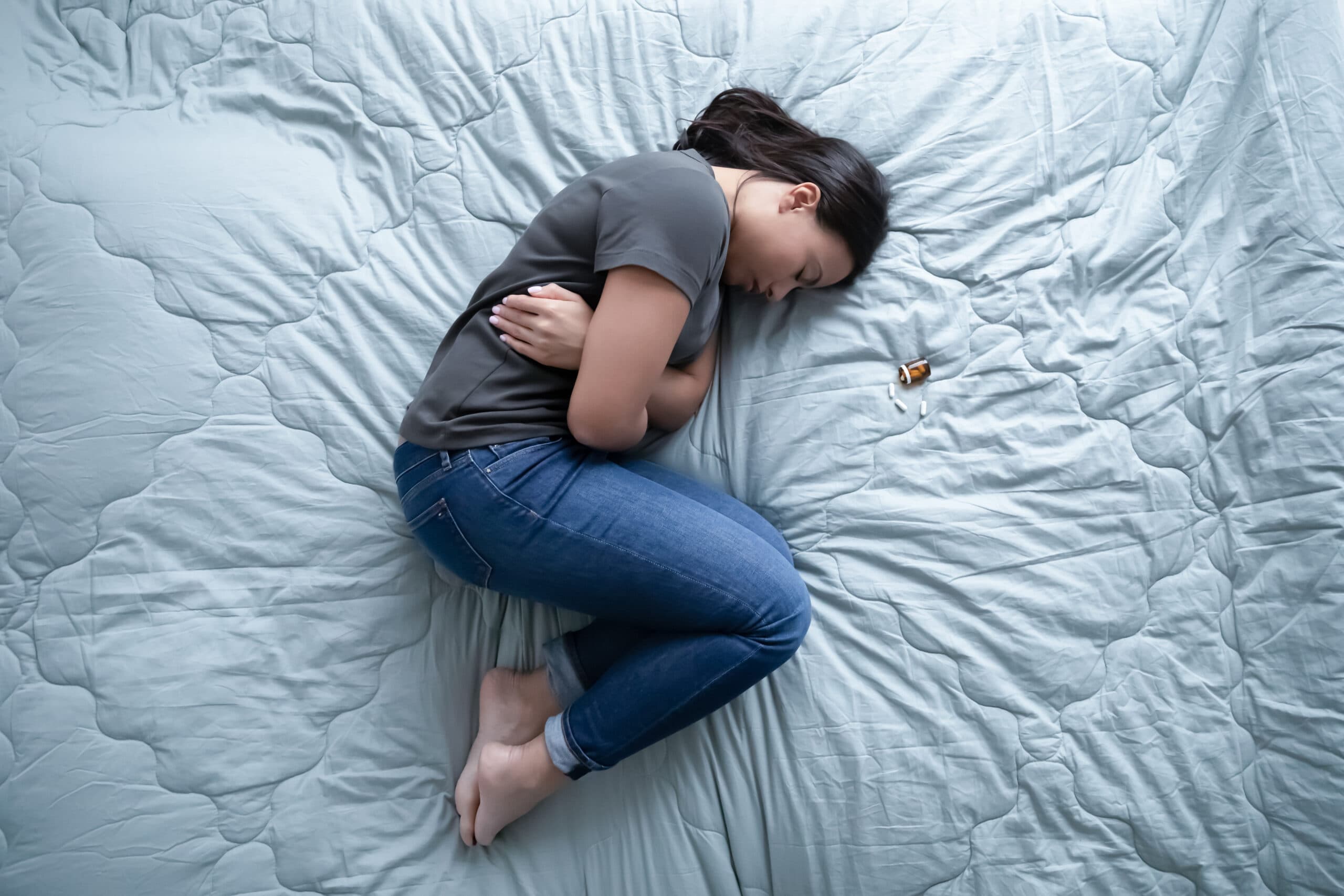 woman laying on bed next to pills