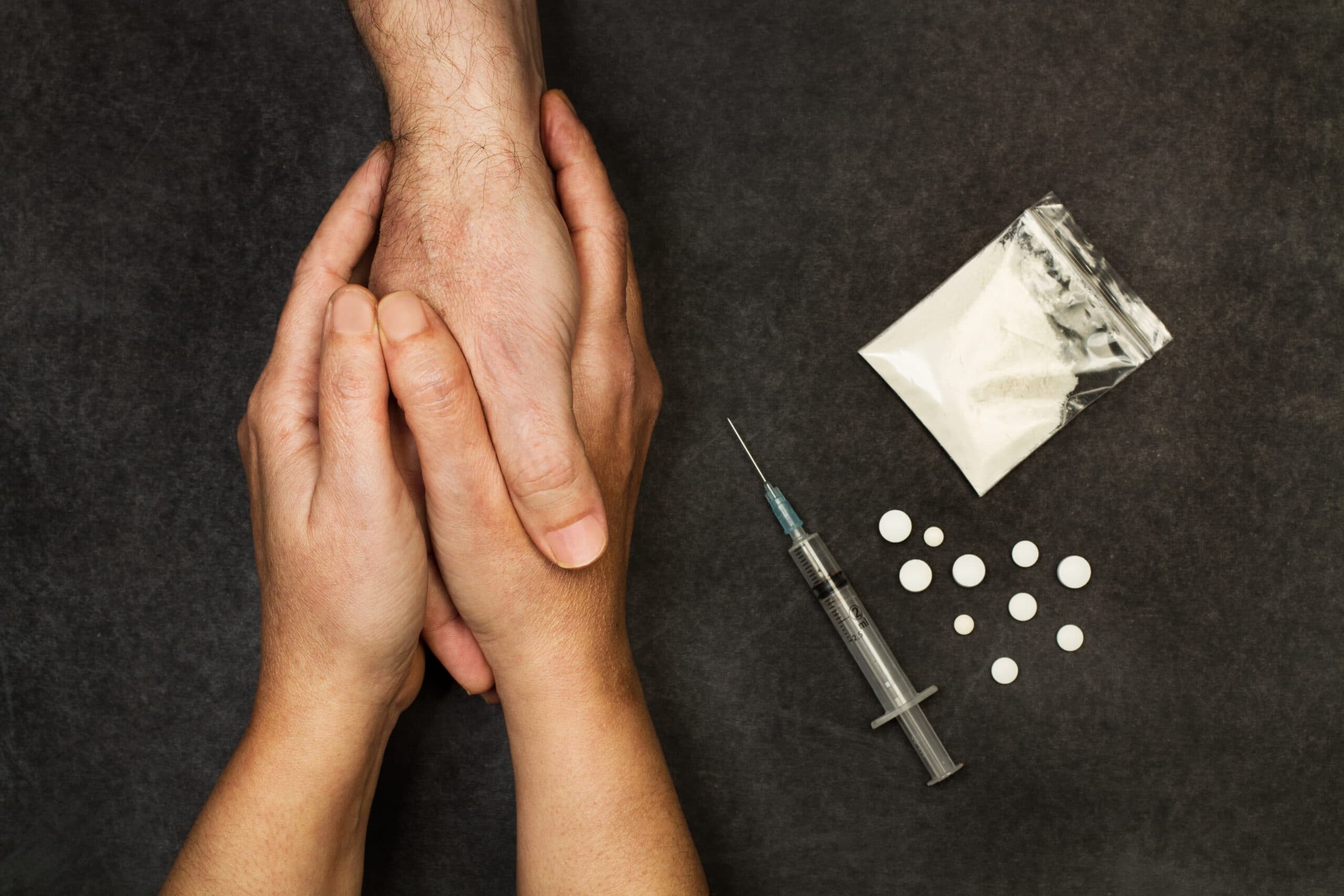 people holding hands next to meth powder drugs needle