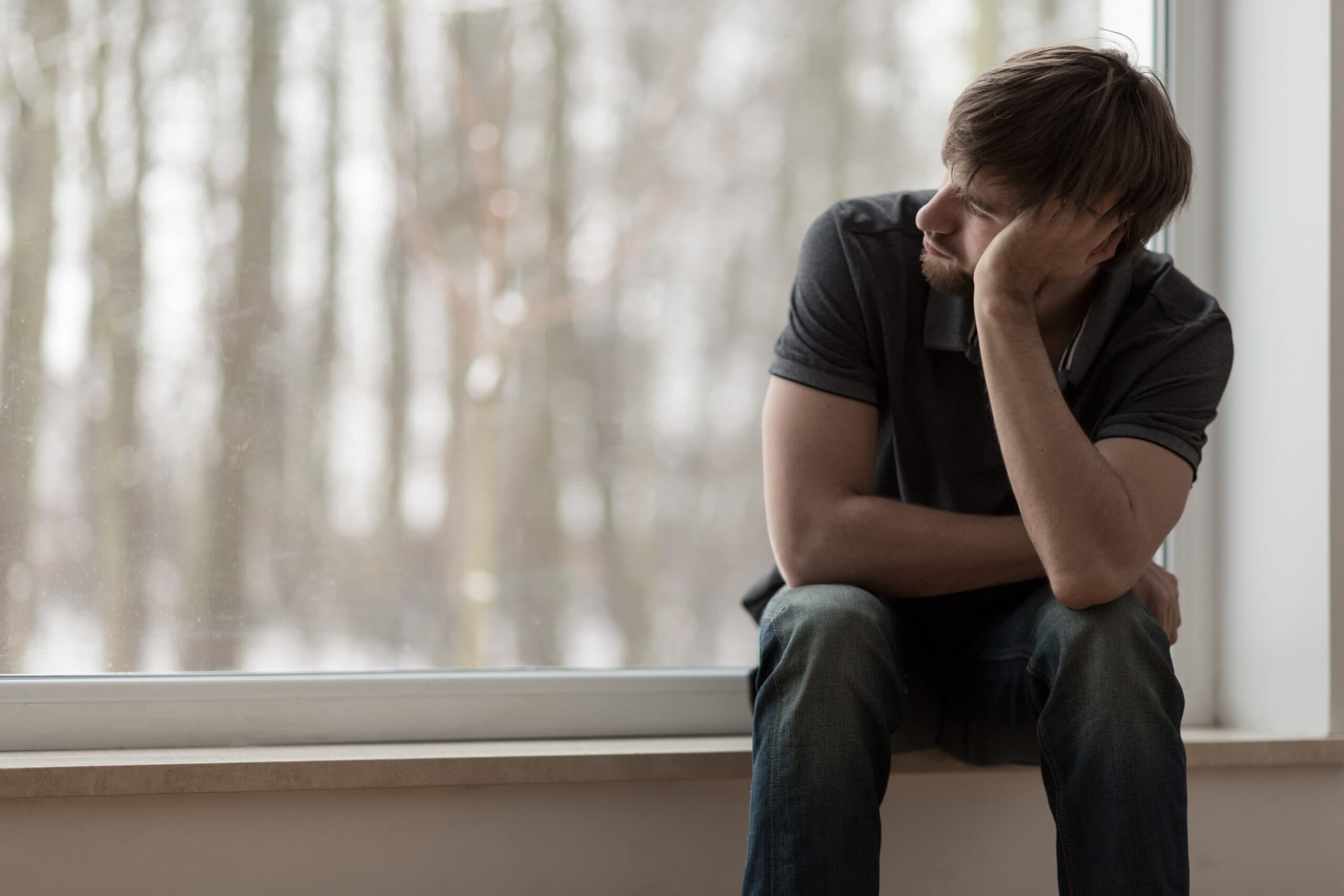 sad young man hungover staring out window