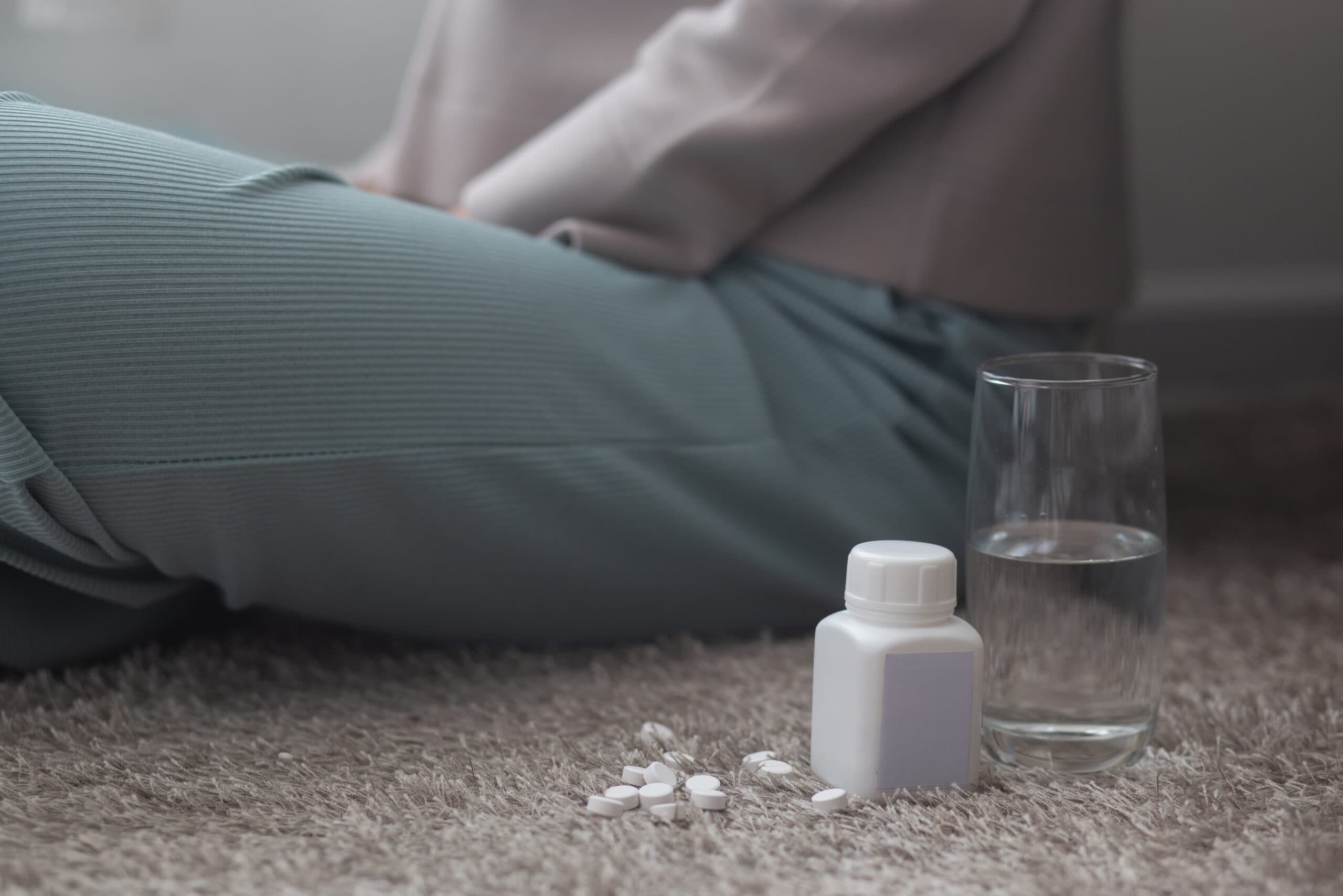 young woman sitting with bottle of pills and water