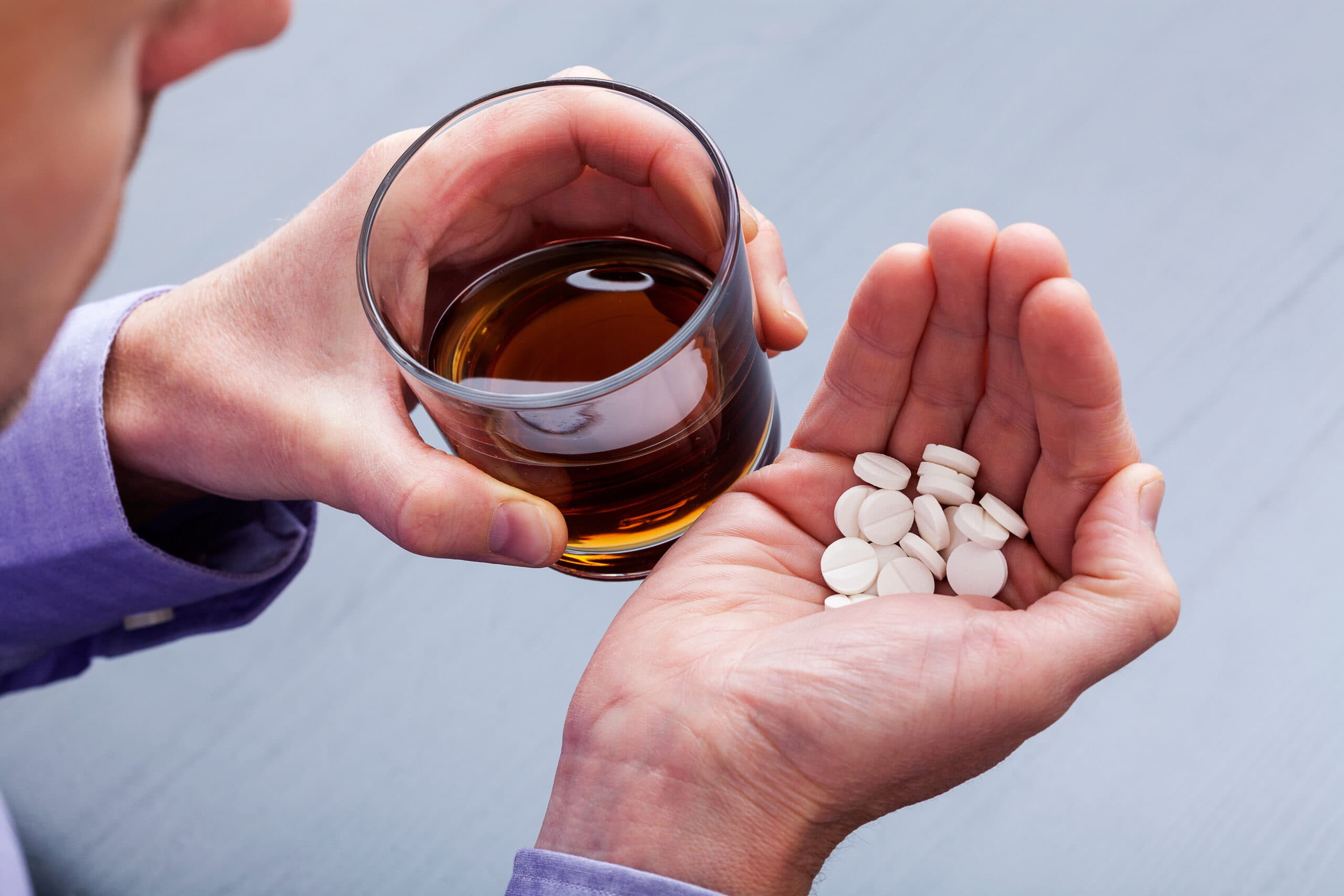 man holding liquor glass and white pills