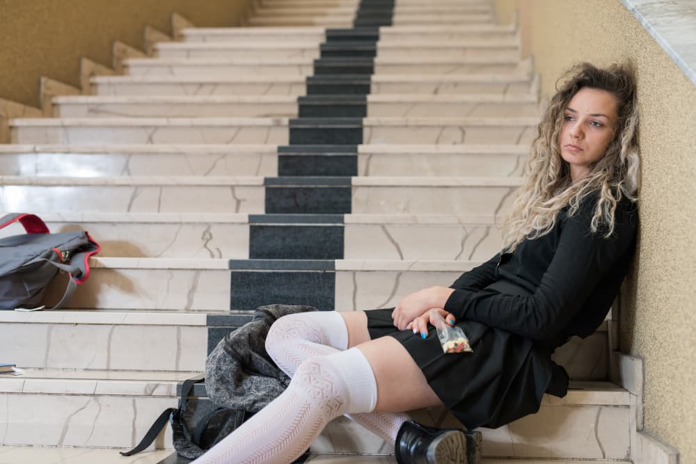 young girl sitting on steps with bag of pills