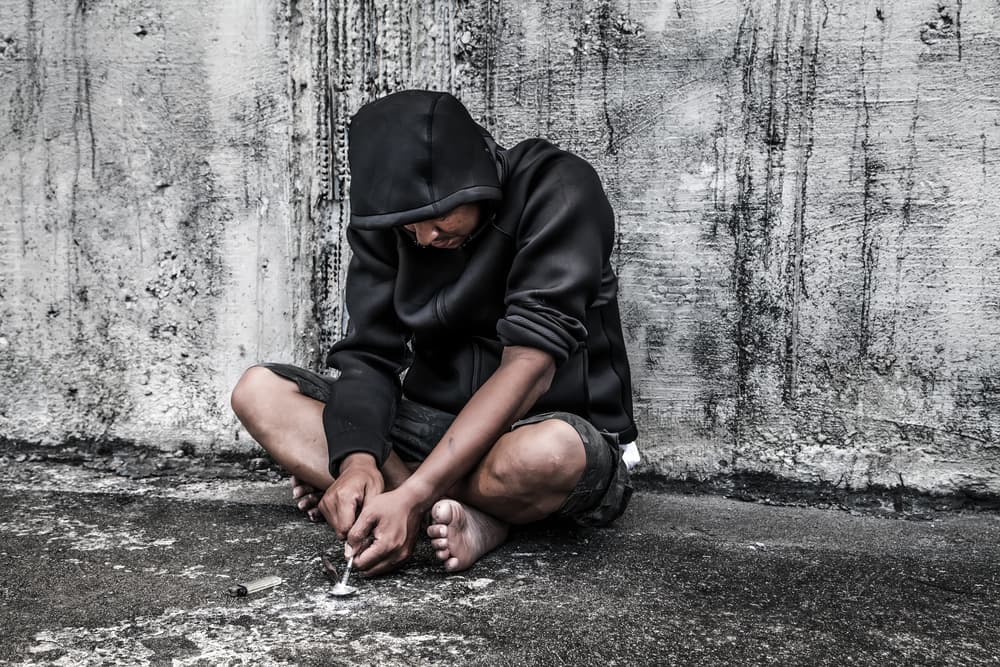 young man drug addict with needle sitting on street