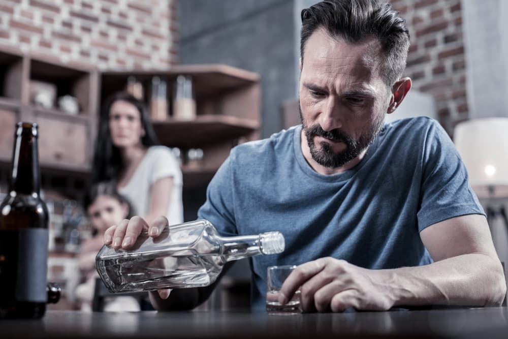 man drinking liquor with wife and son sad