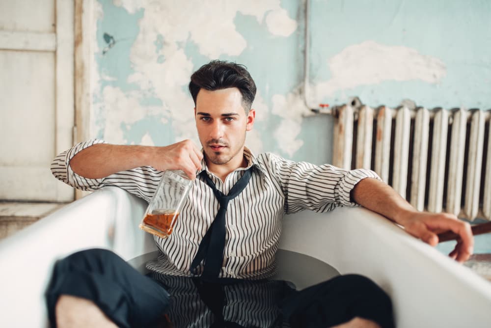 drunk man in suit in bathtub with bottle of liquor