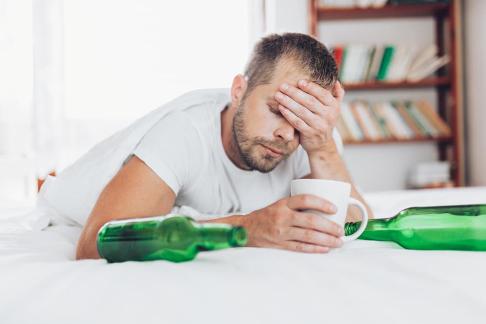 man hungover with beer bottles drinking coffee