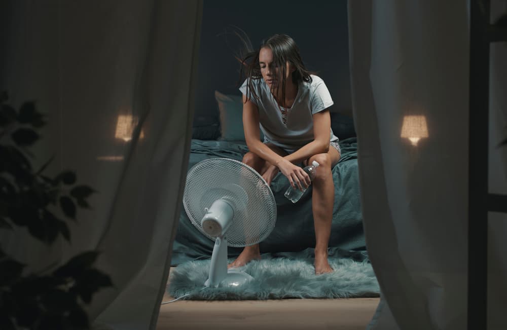 woman with night sweats hot tired with water and fan