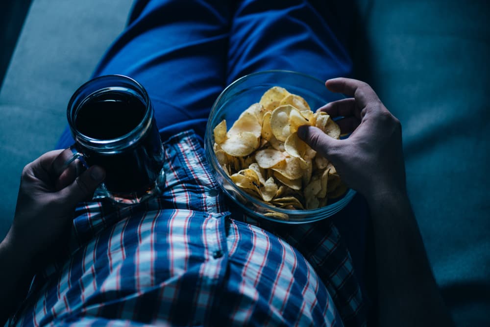 man laying down drinking beer and eating chips