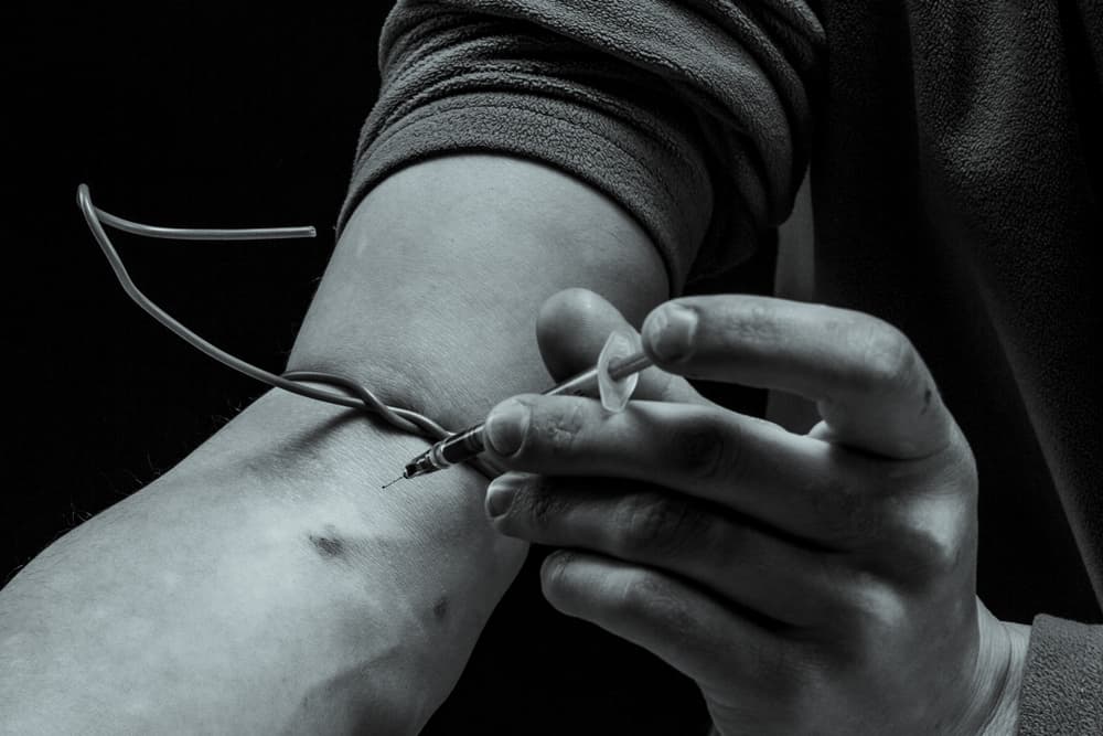 person injecting drugs in arm track marks