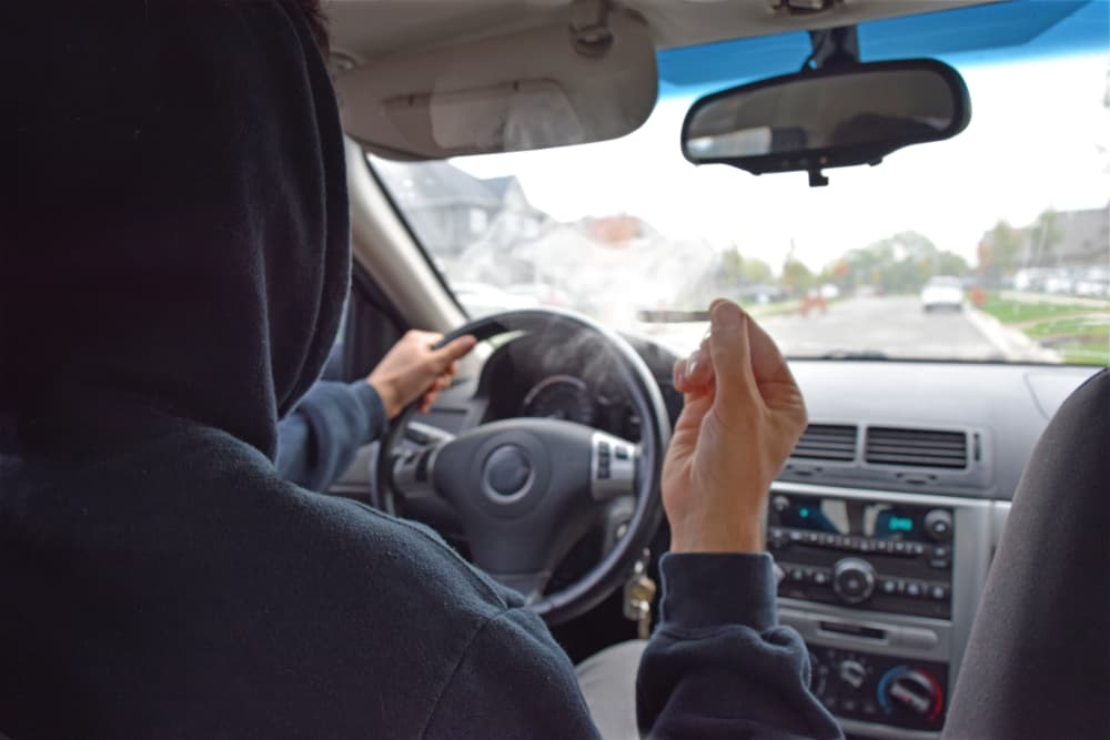 man driving car while smoking joint of weed hot boxing