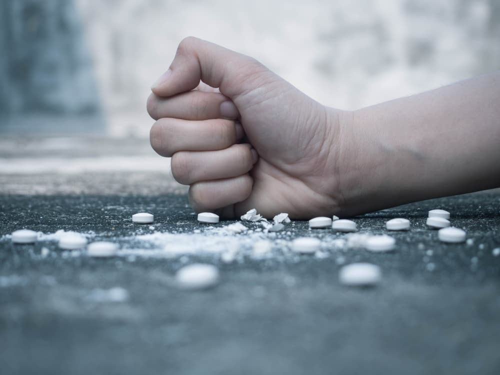 Young human hand crushing white pills with fist