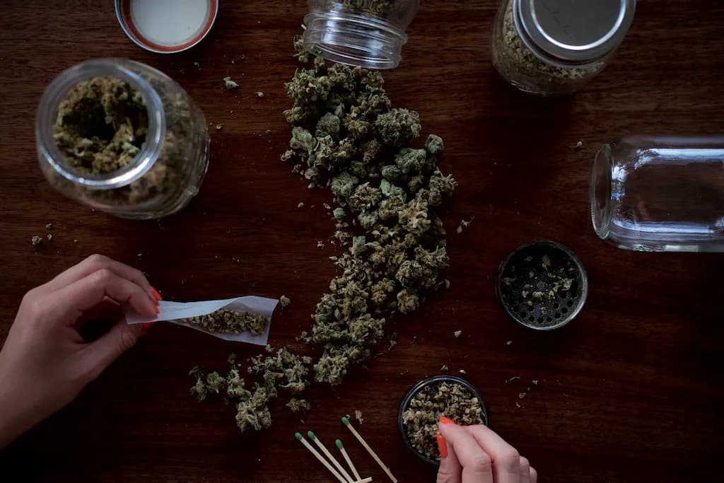 marijuana buds on table and in jars hands rolling joint