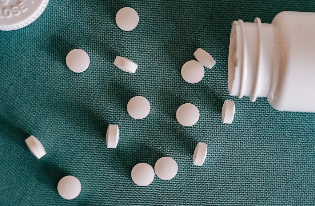 Top view of similar small round white pills spilled from plastic container on green surface