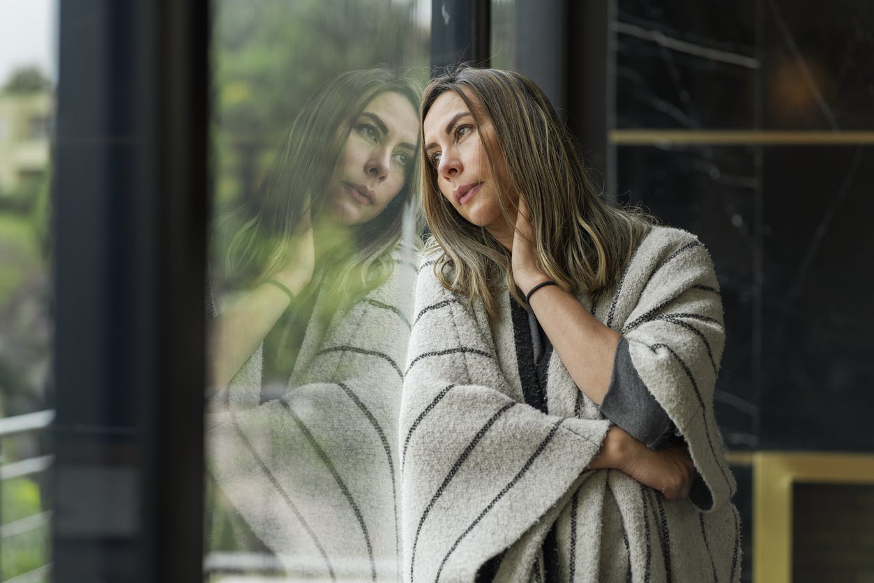 bored and sad woman leaning against window looking outside