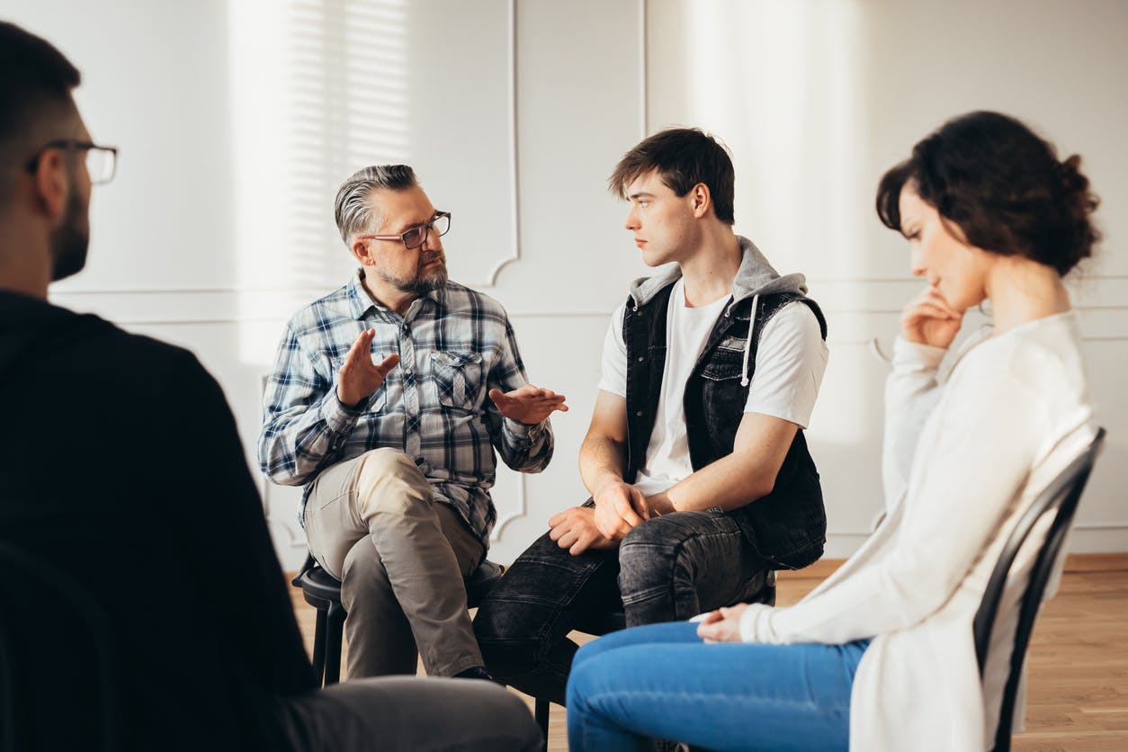 Psychologist talking about twelve-step program to addicted man during group support meeting