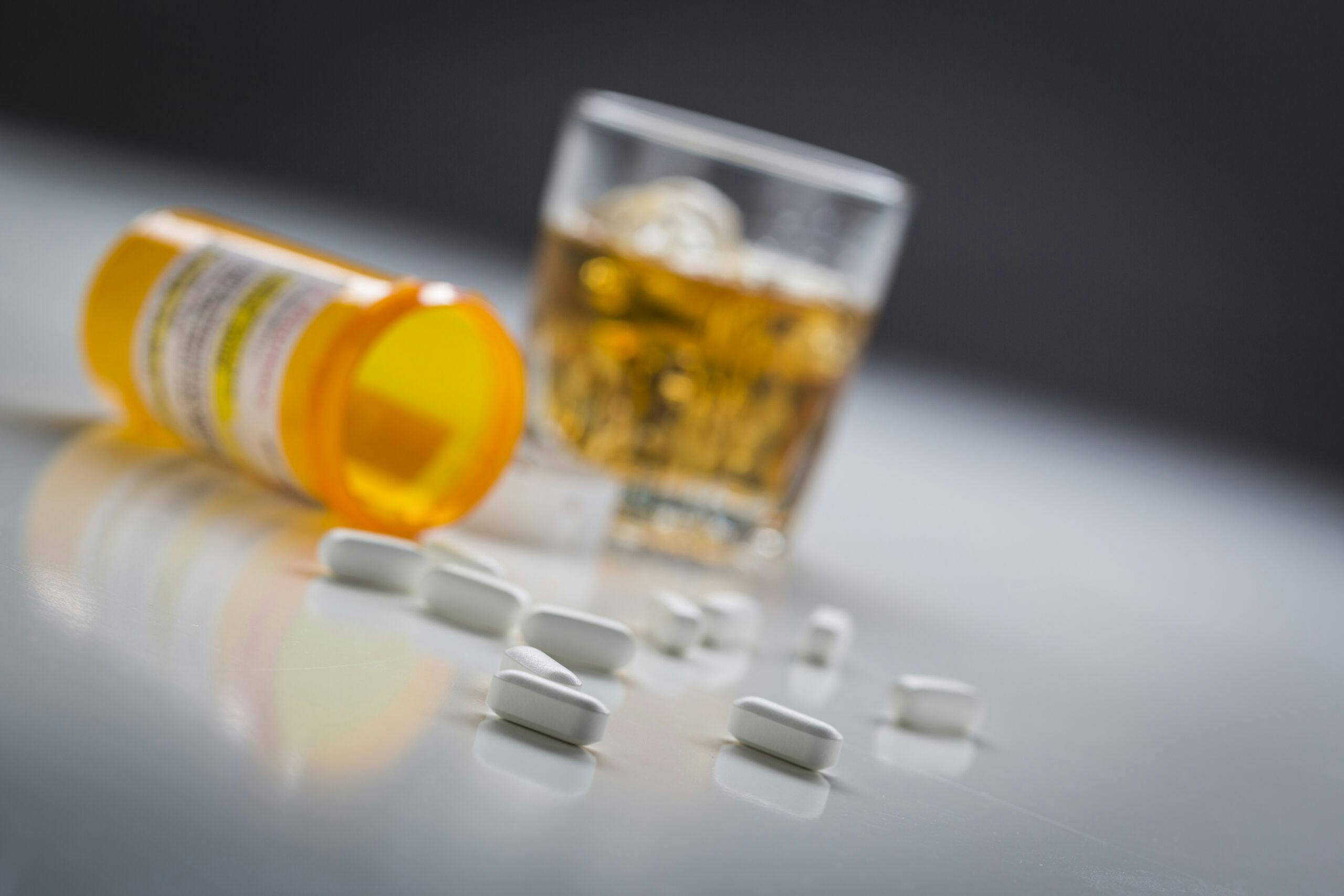 white prescription pills spilled out with glass of liquor