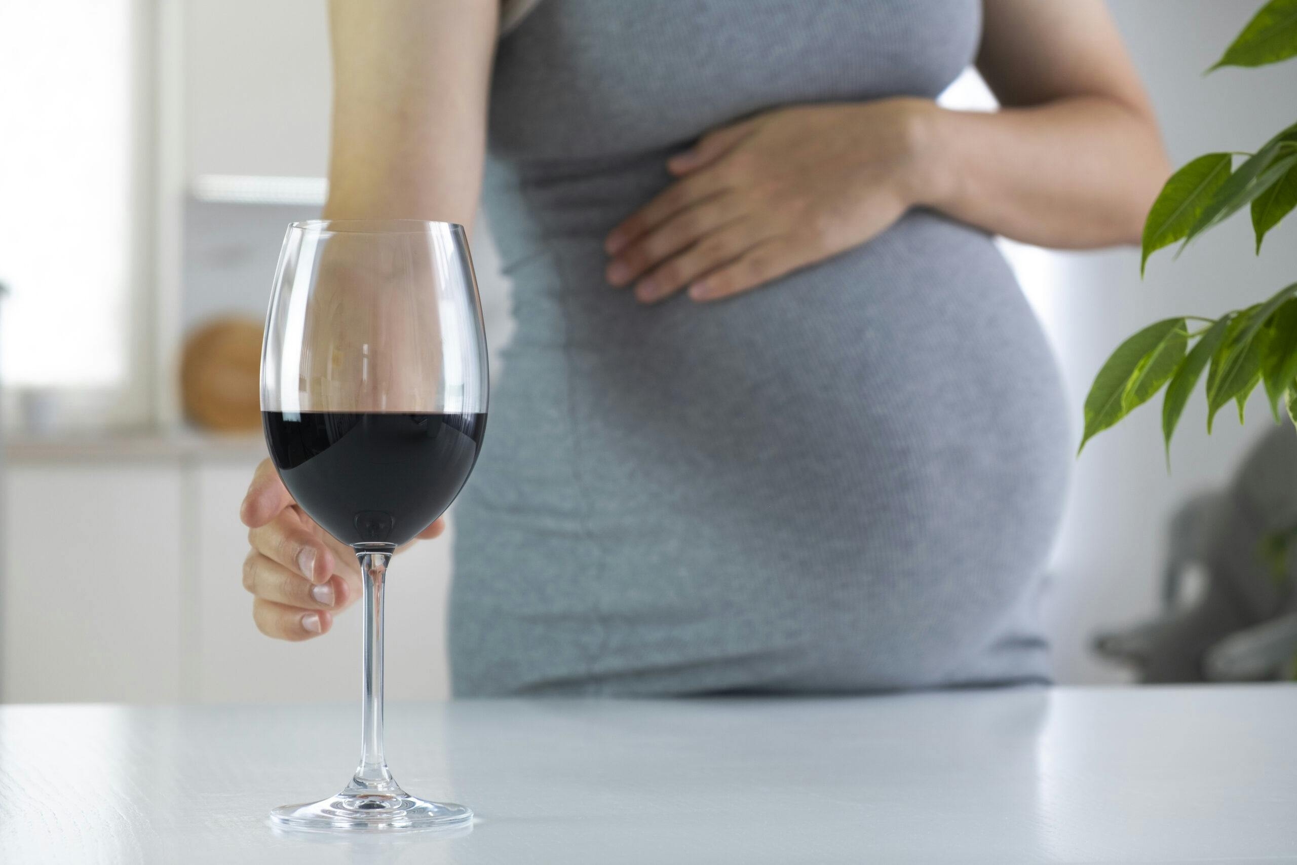 pregnant woman with hand on belly holding glass of wine