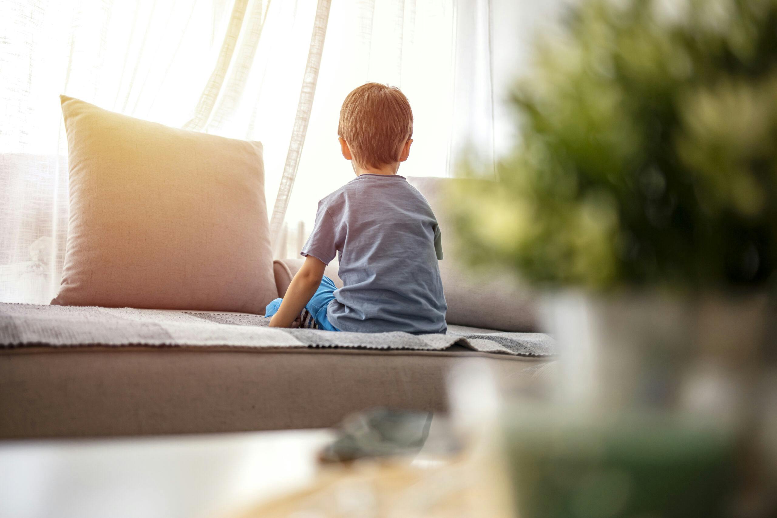 little boy sitting on couch looking out window