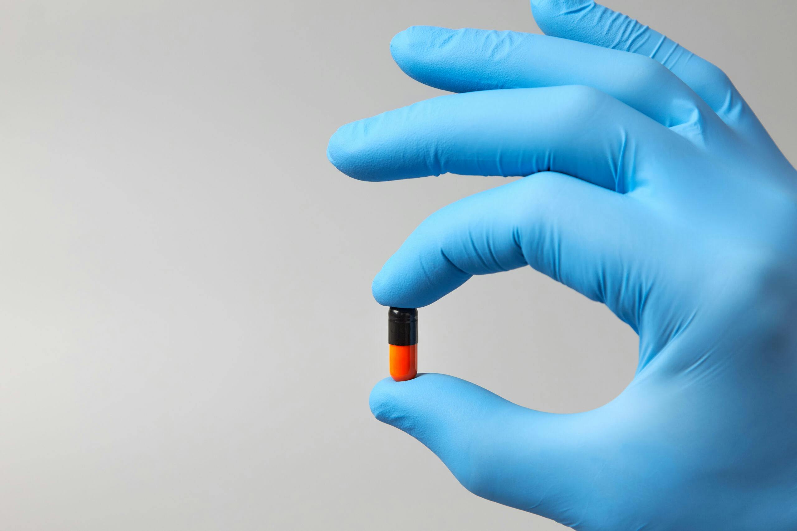 blue glove hand holding orange and black capsule pill