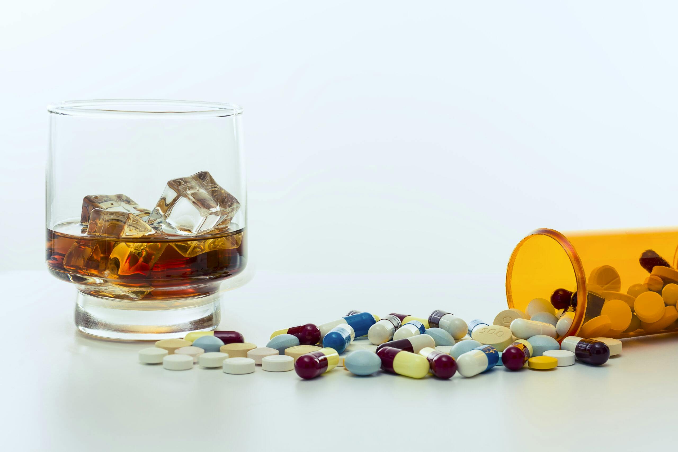 whiskey in glass with pills spilling out of bottle