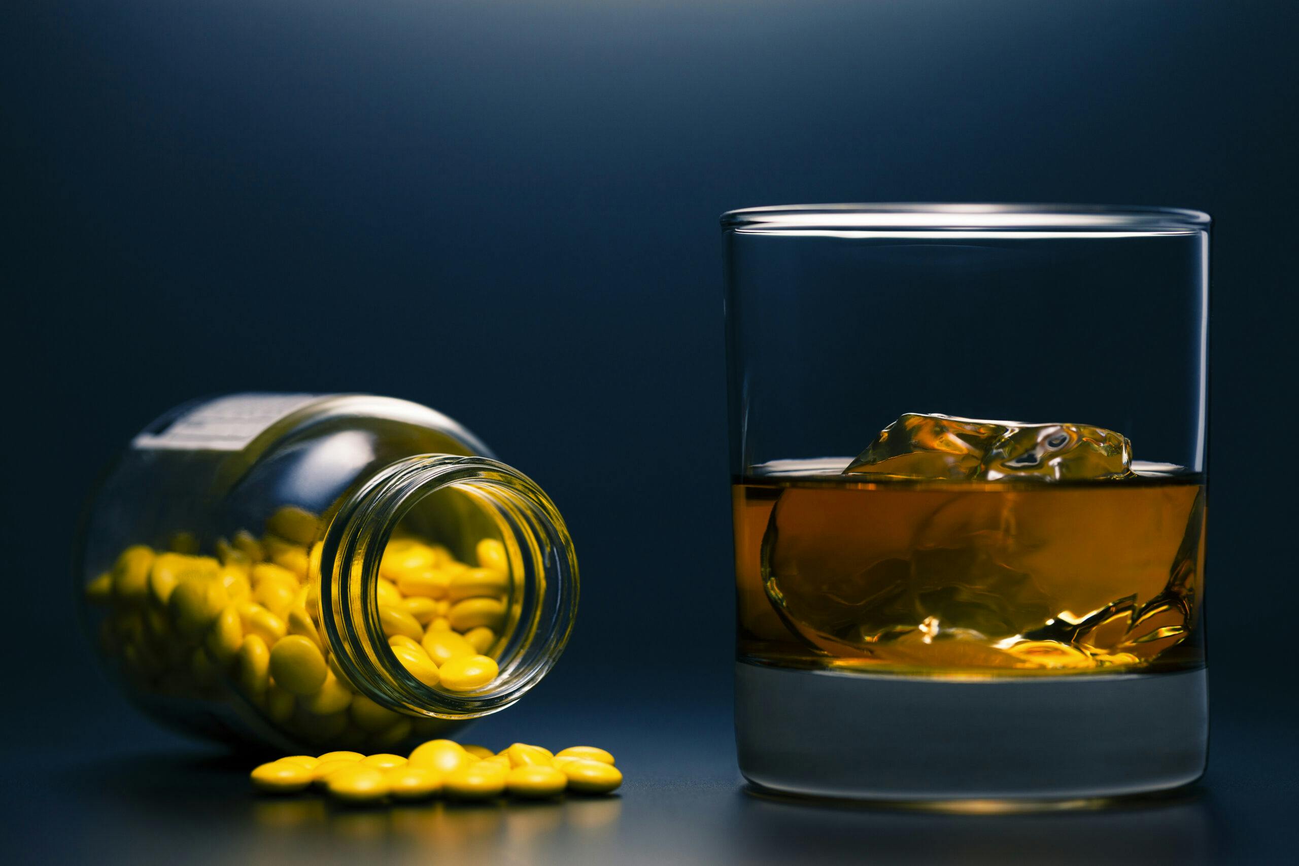 liquor drink in glass with pills spilled from bottle