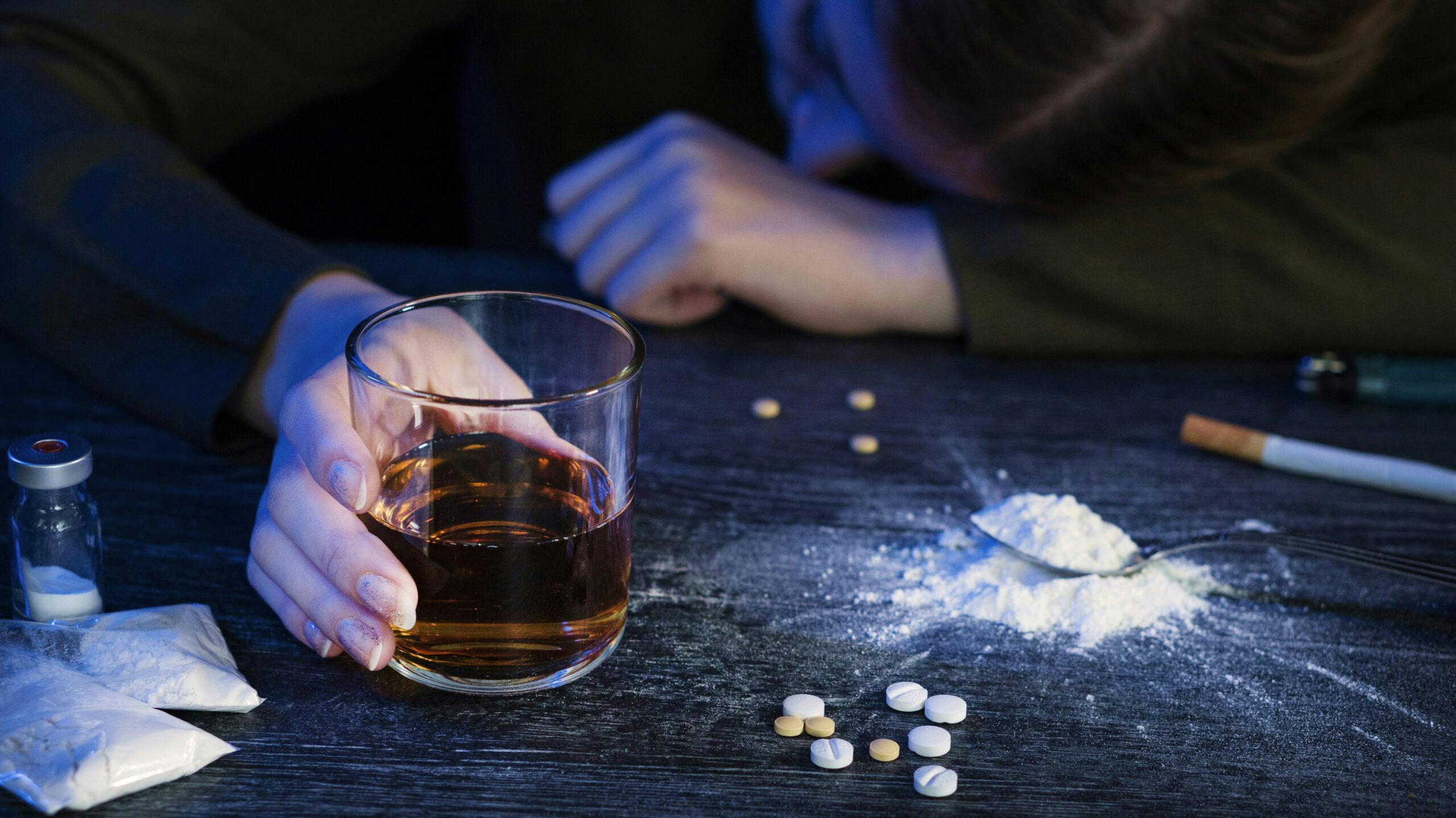 person laying down drinking liquor with powder drug and pills