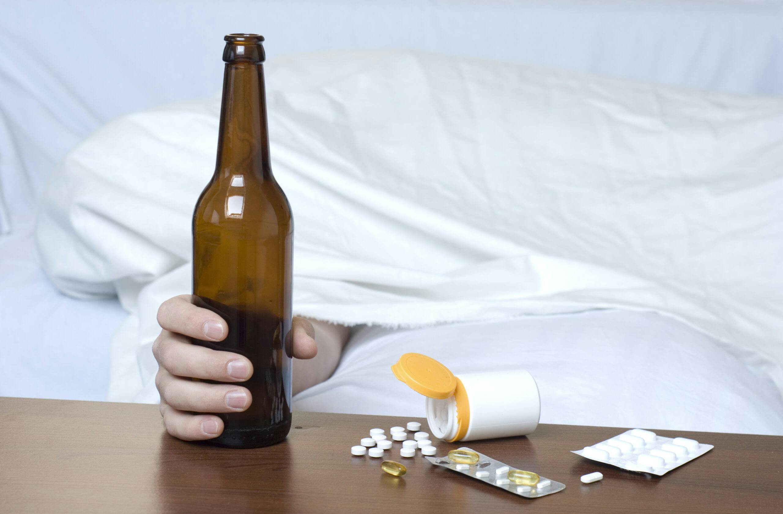 beer bottle with various pills on table man sleeping in bed