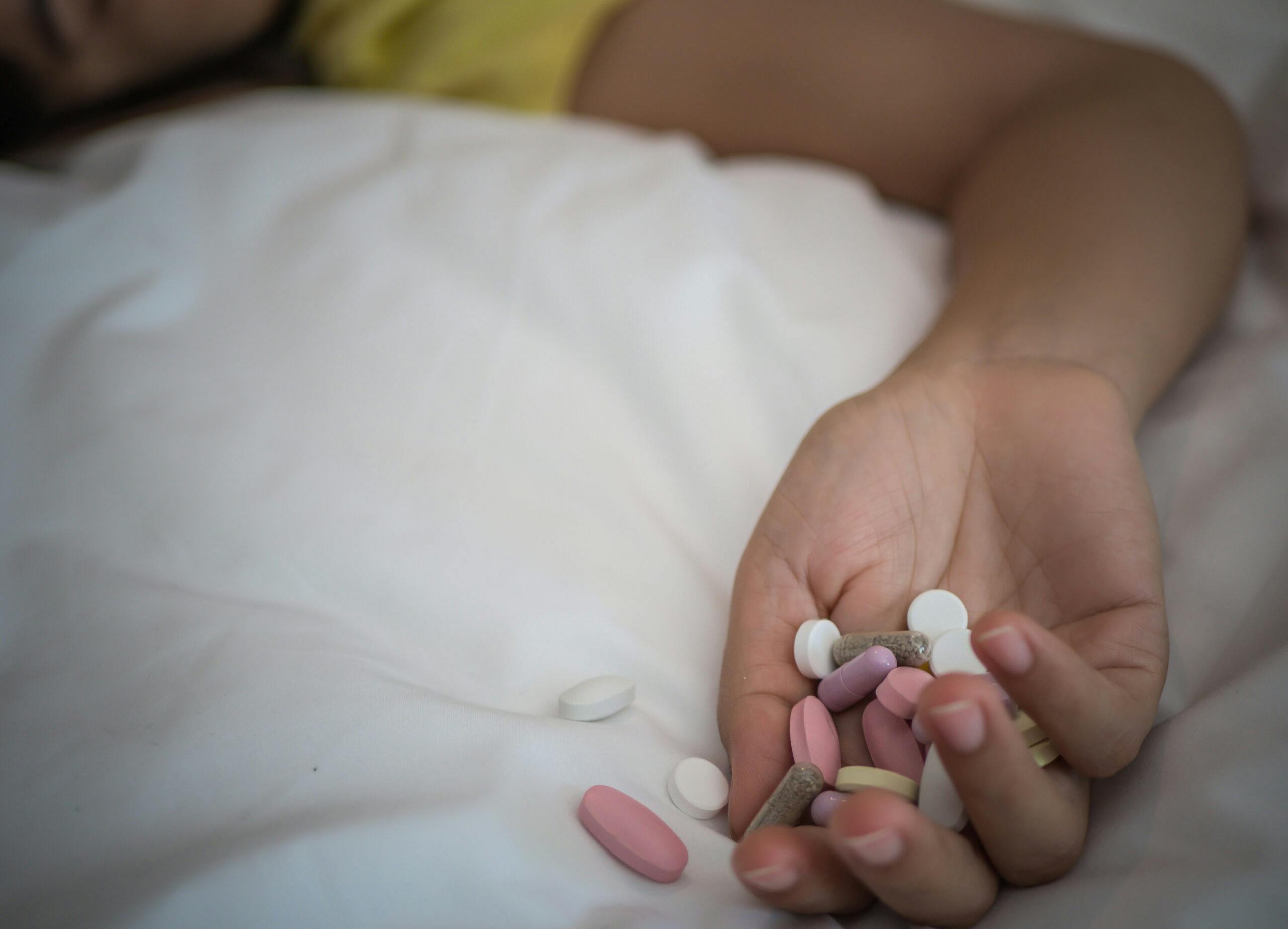 woman lying on bed with pills in hand overdose