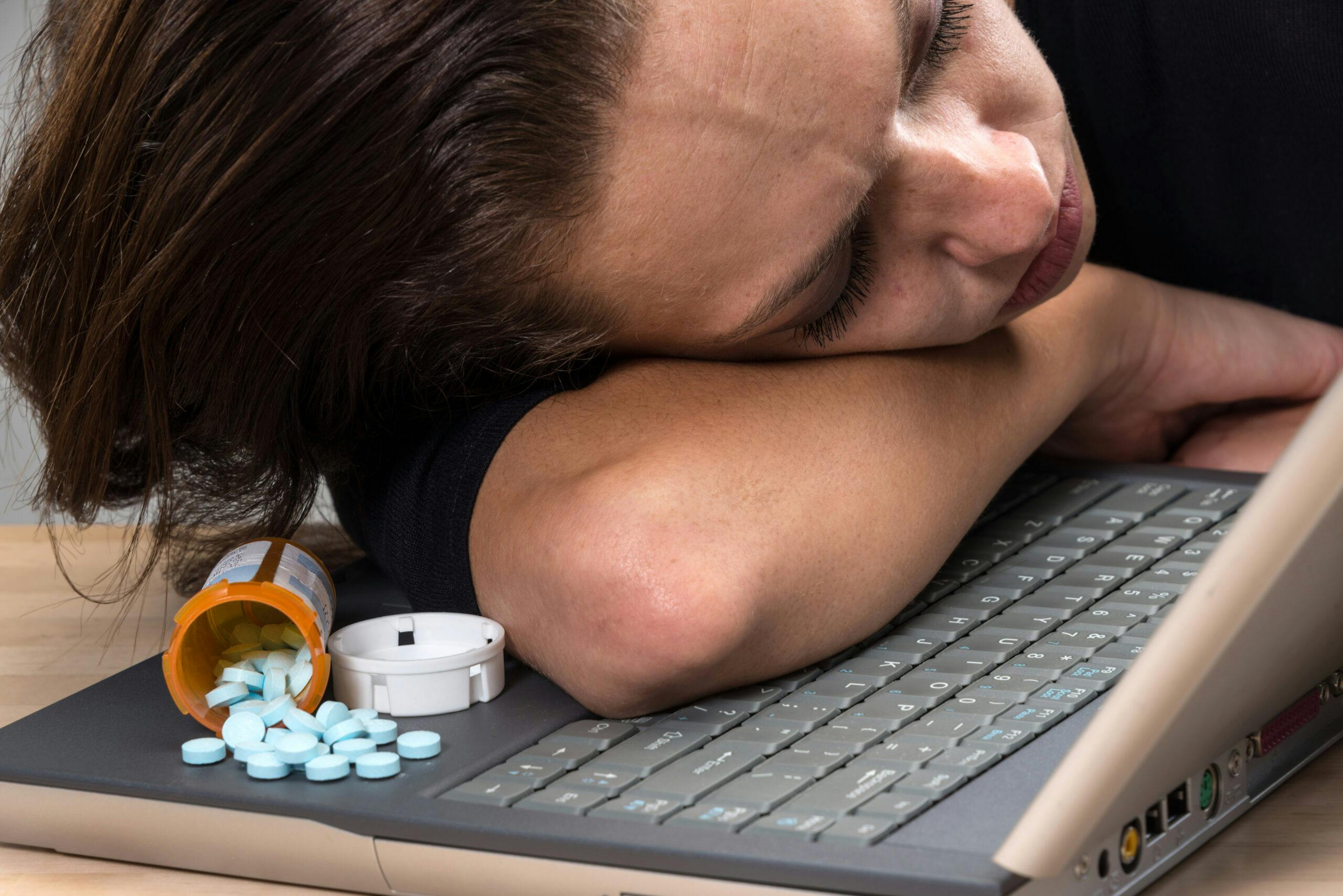 woman sleeping on laptop next to alprazolam pills spilled
