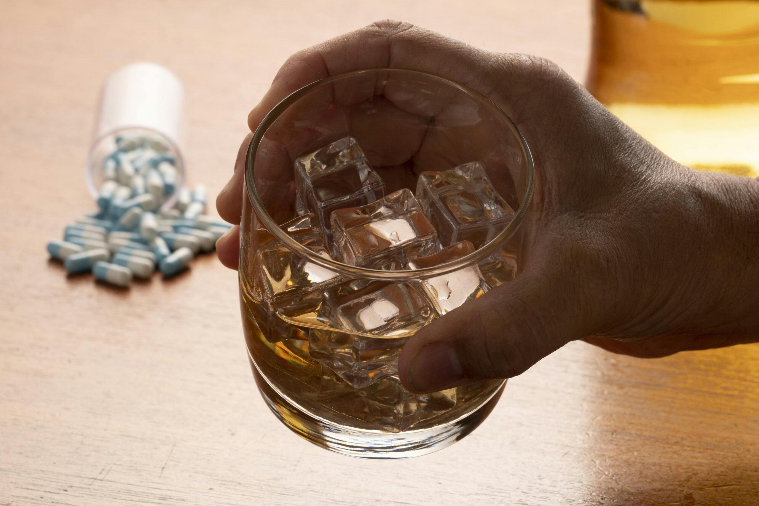 man holding glass of whiskey with capsule pills