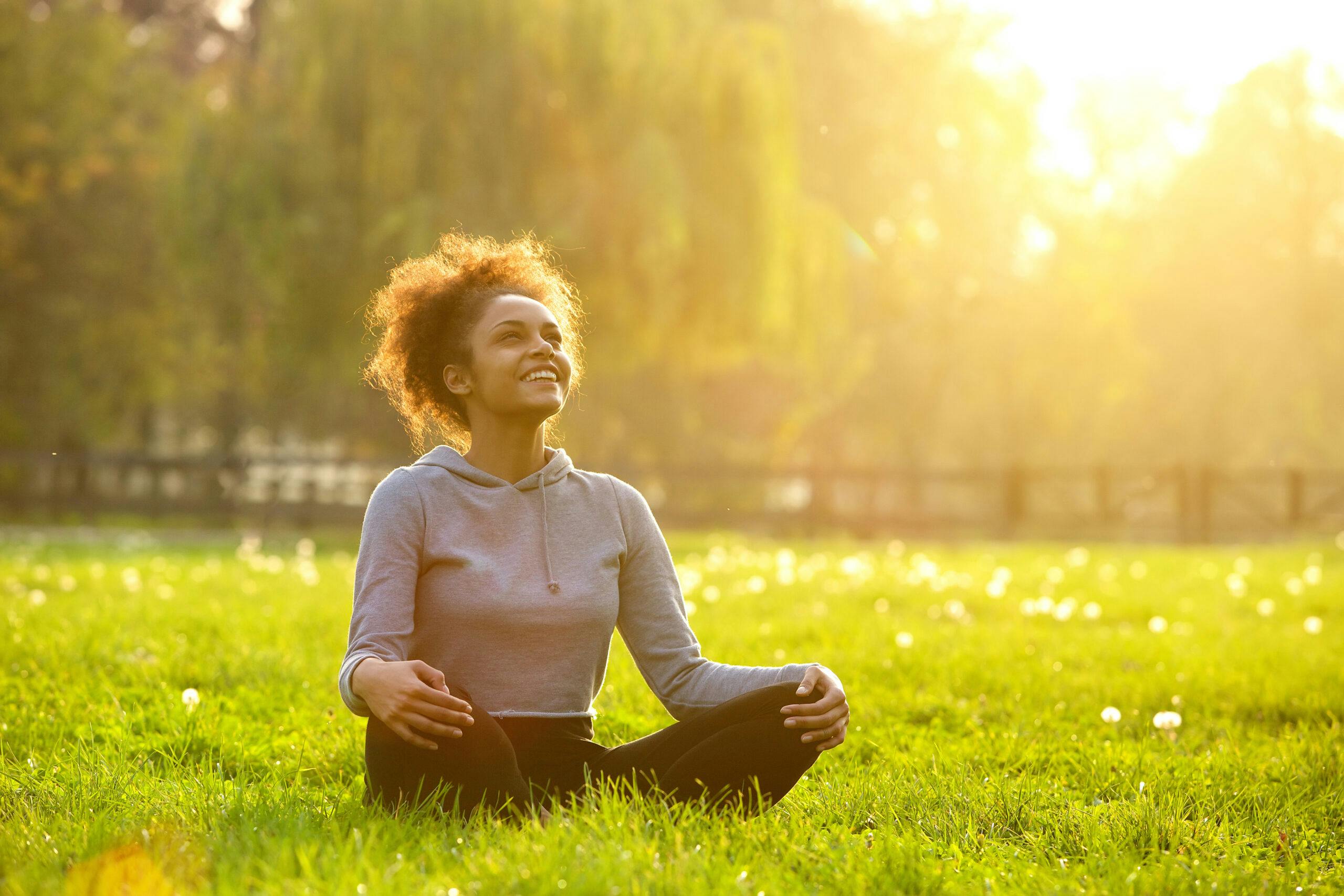 happy woman sitting meditating in grass