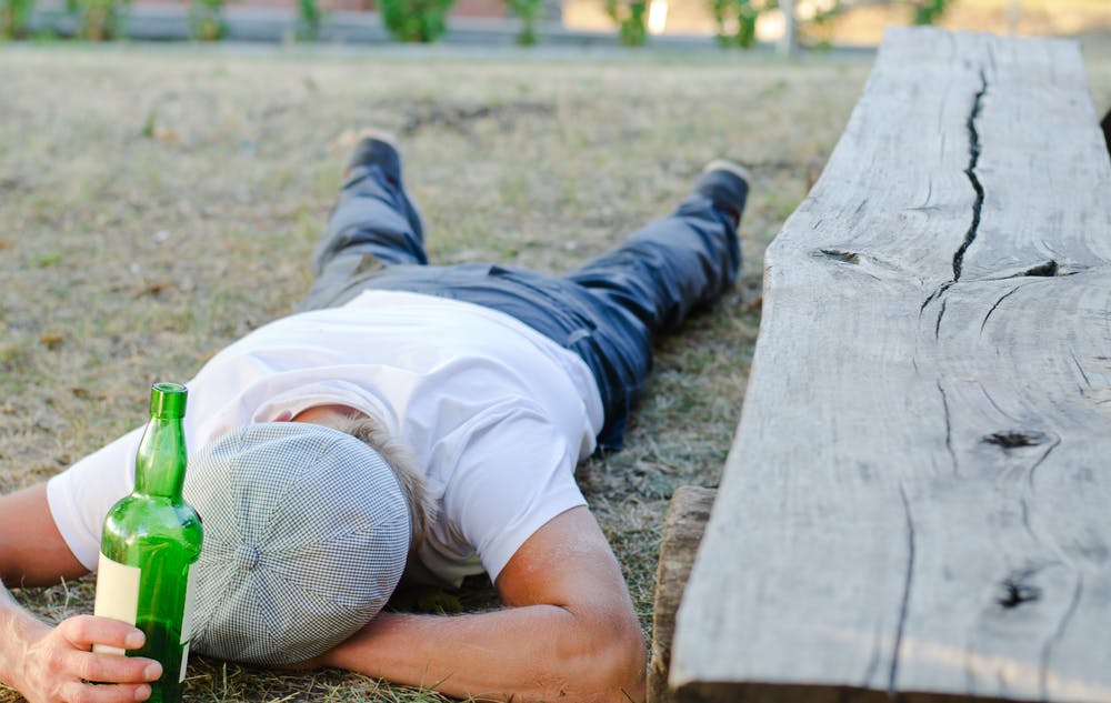 man sleeping on ground with liquor bottle in hand