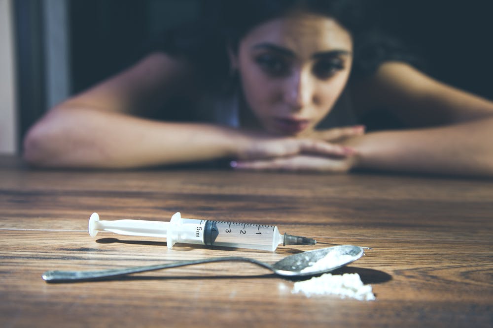 woman looking at drugs and needle considering relapse