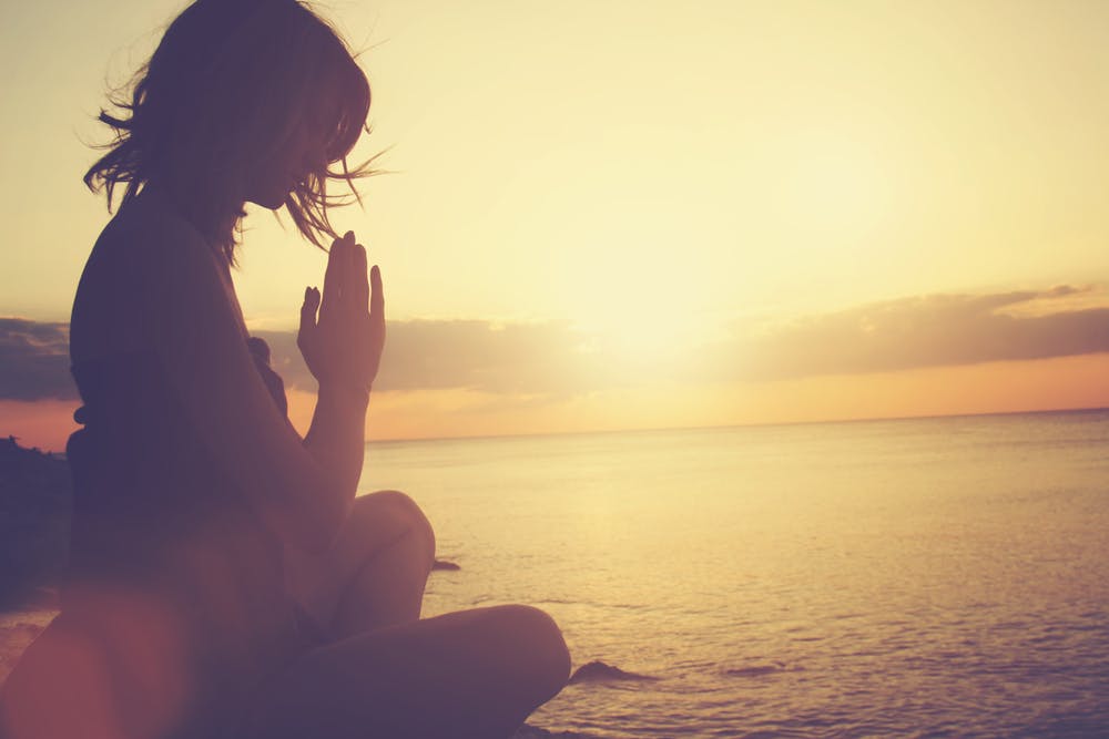 woman praying by sunrise beach