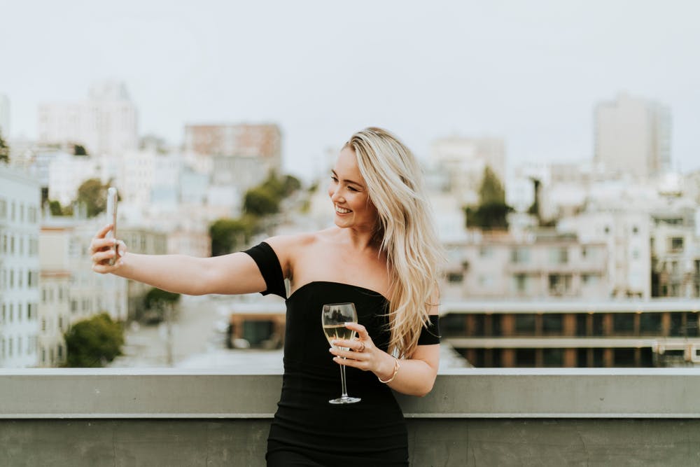 woman taking selfie drinking wine on rooftop