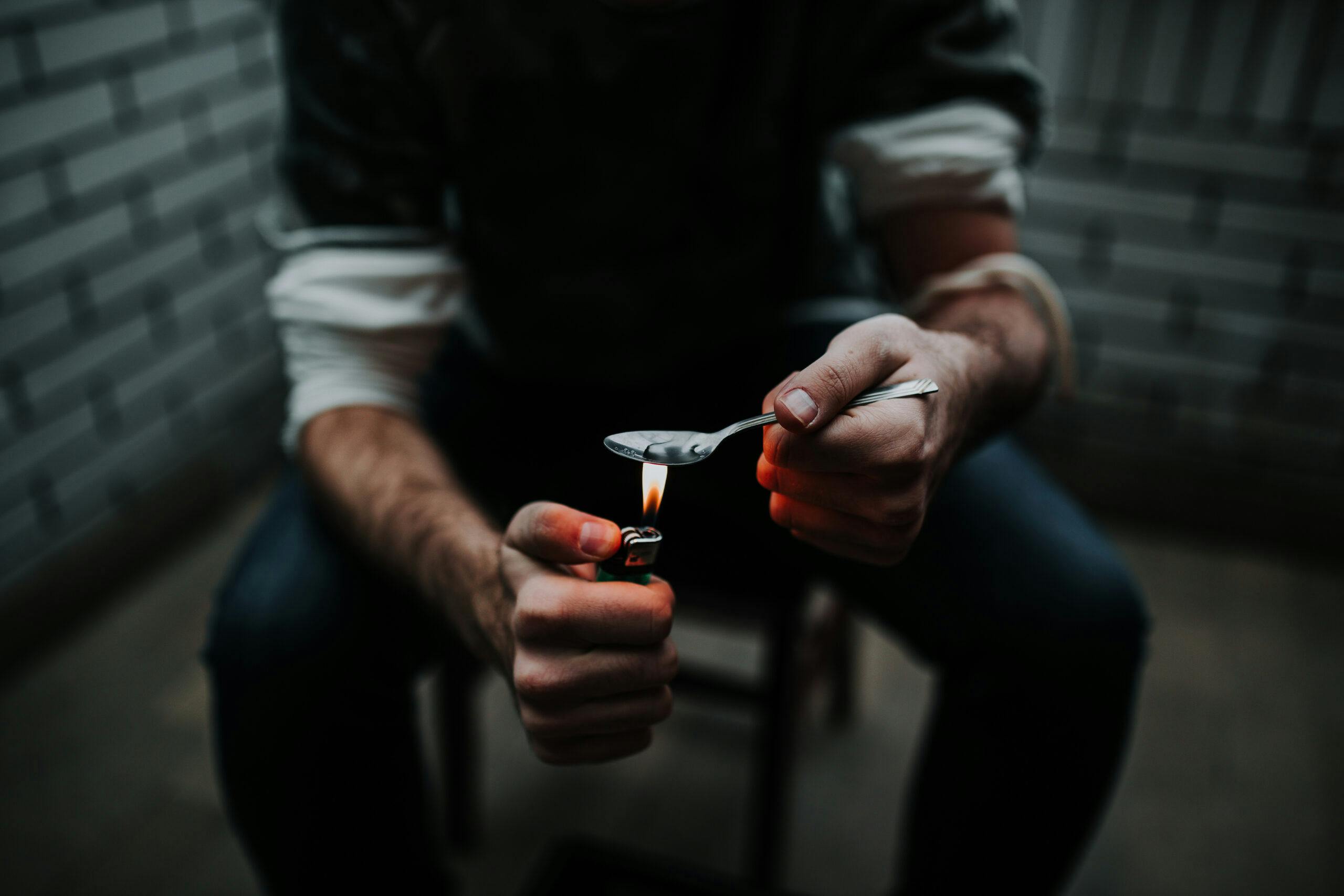 man preparing black tar heroin hit with spoon and lighter