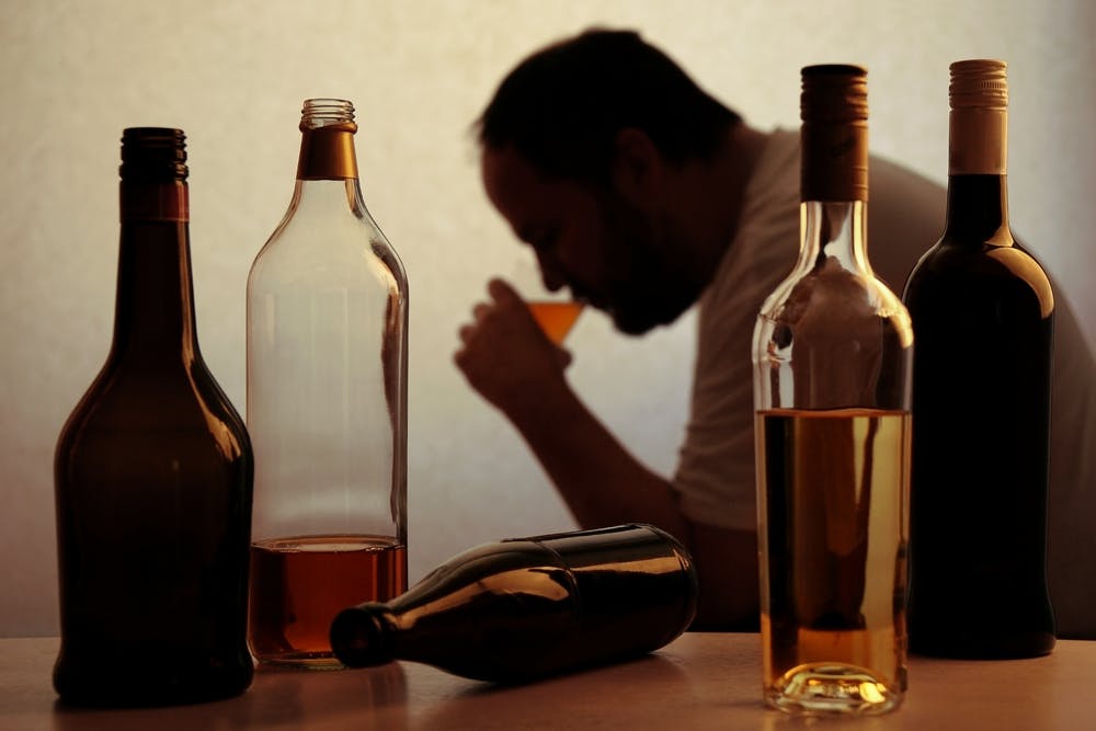 alcoholic man surrounded by bottles of liquor
