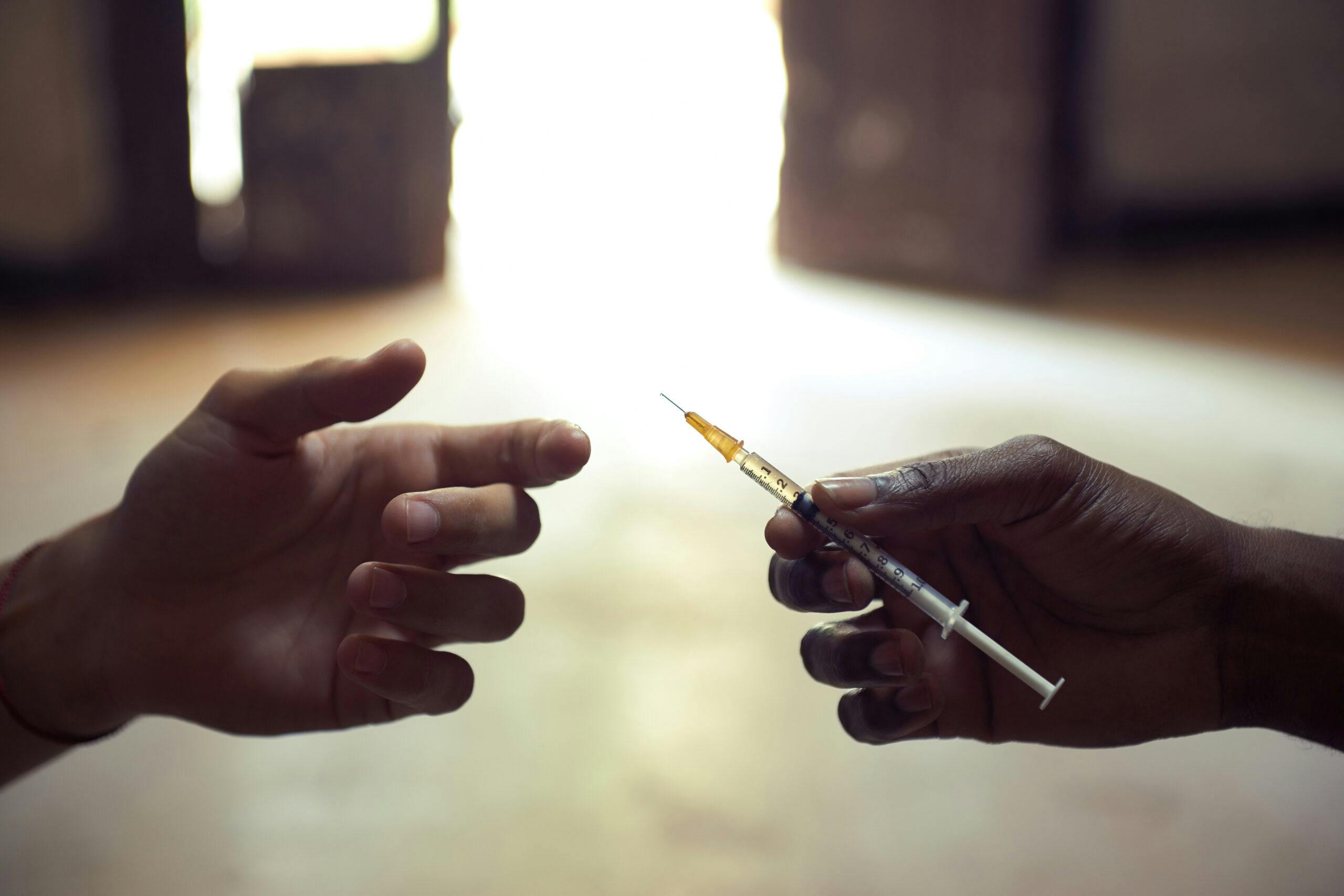 heroin addict with needle handing it to someone