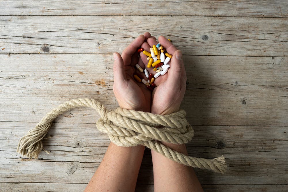 man's hands tied together with rope holding pills