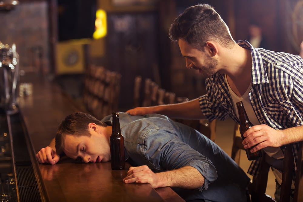 drunk man head down on bar friend trying to wake him